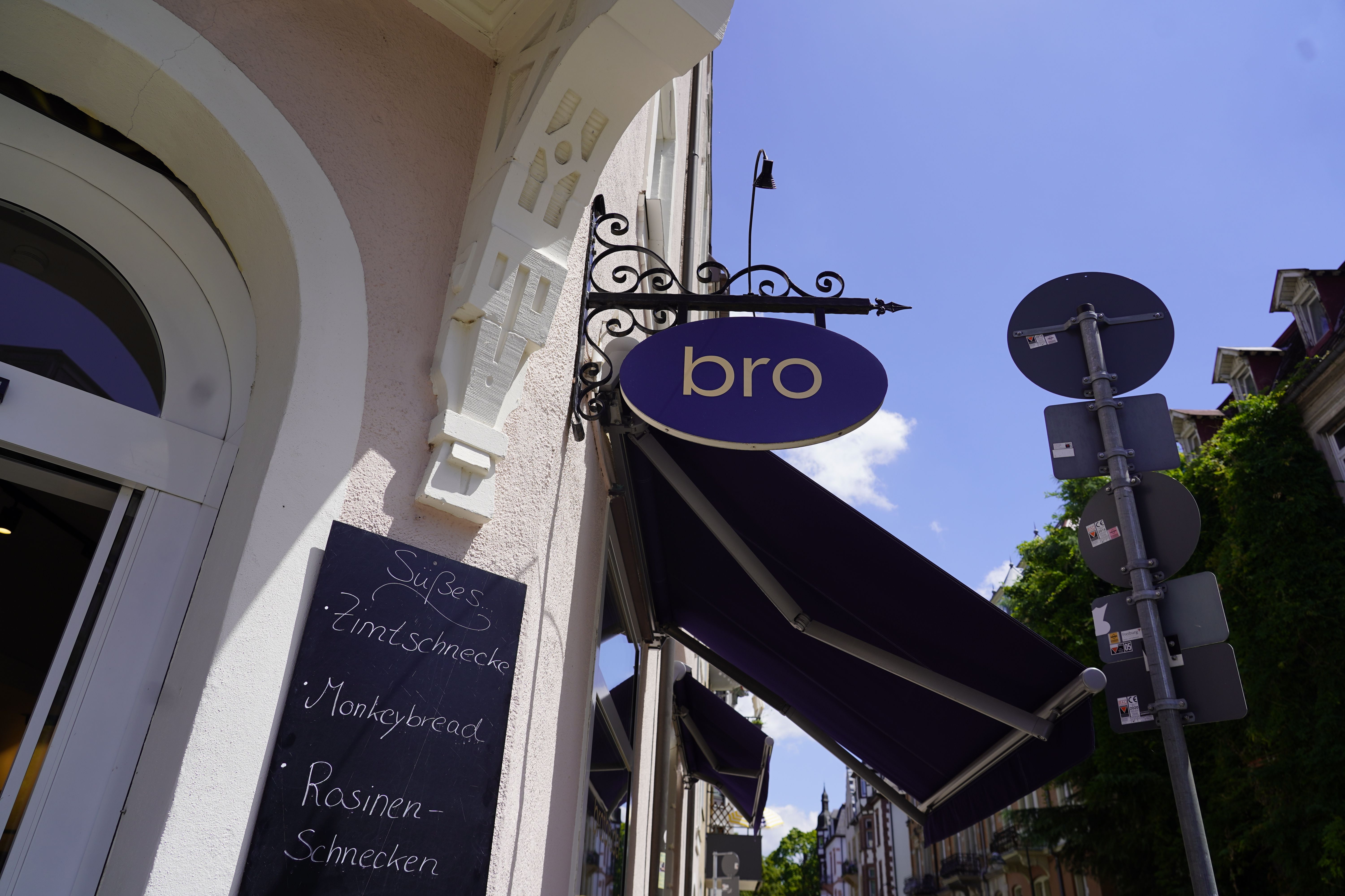Außenansicht eines Cafés mit einem Schild 'bro' und einer Tafel, die Zimtschnecken, Monkeybread und Rosinenschnecken anbietet.