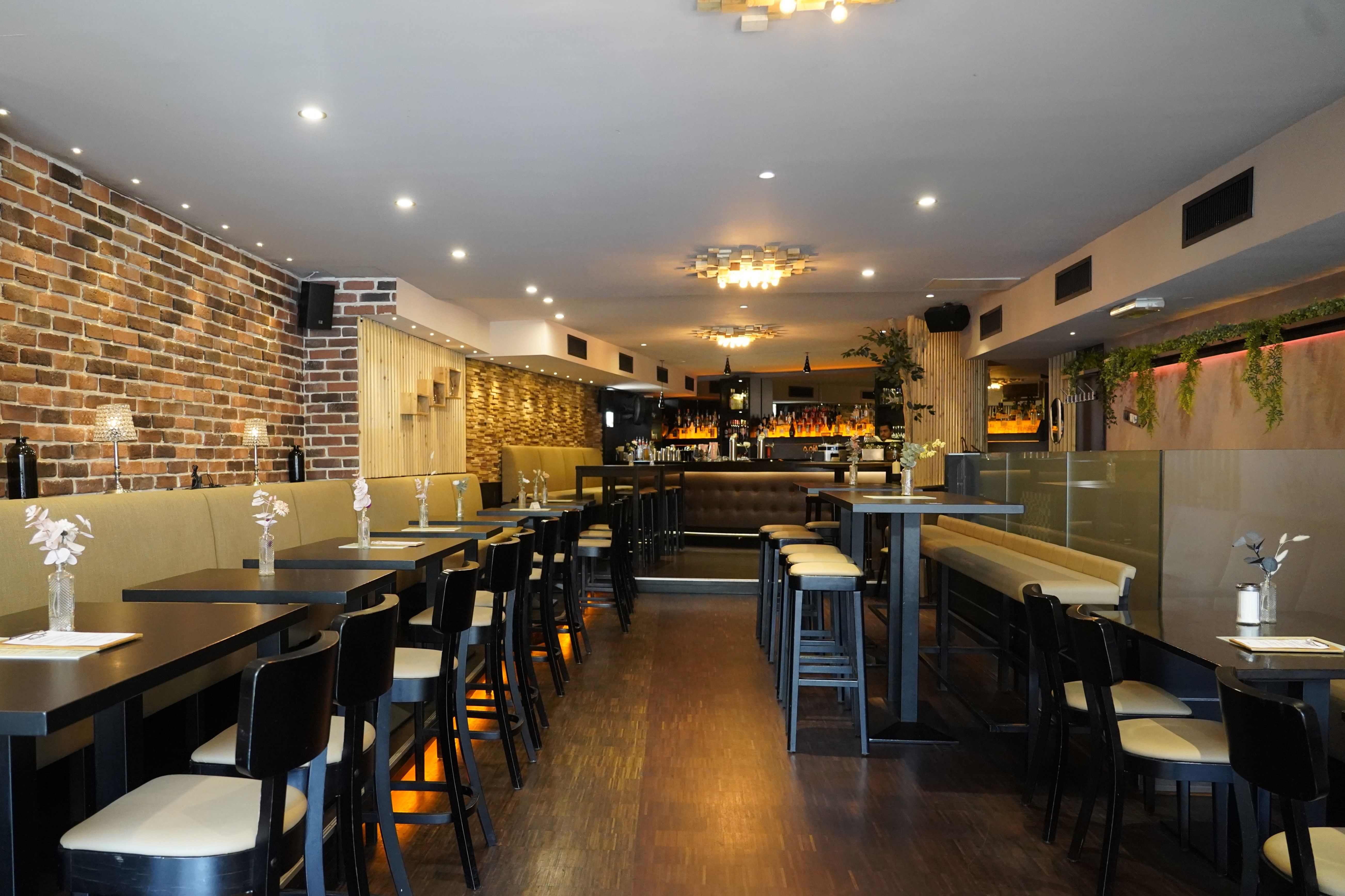 Modernes Restaurant mit Backsteinwand, stilvollen Tischen und Stühlen, dezenter Beleuchtung und Bar im Hintergrund.
