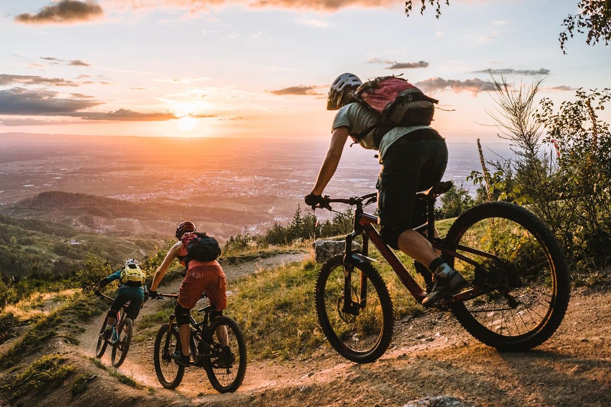 Drei Personen bei einer Trail-Abfahrt im Sonnenuntergang.
