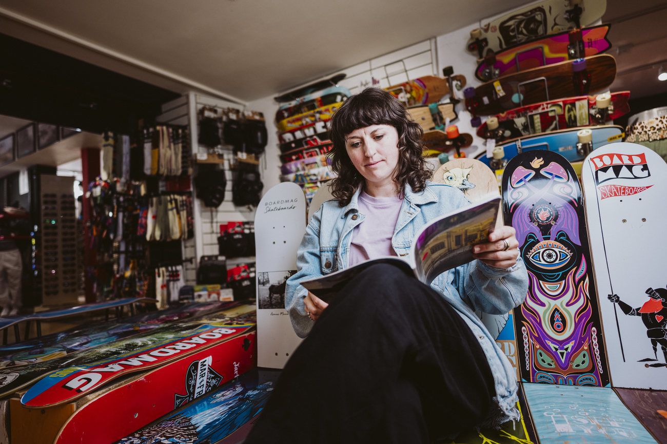 Frau liest im Freiburg-Boardshop zwischen bunten Skateboards und Zubehör.