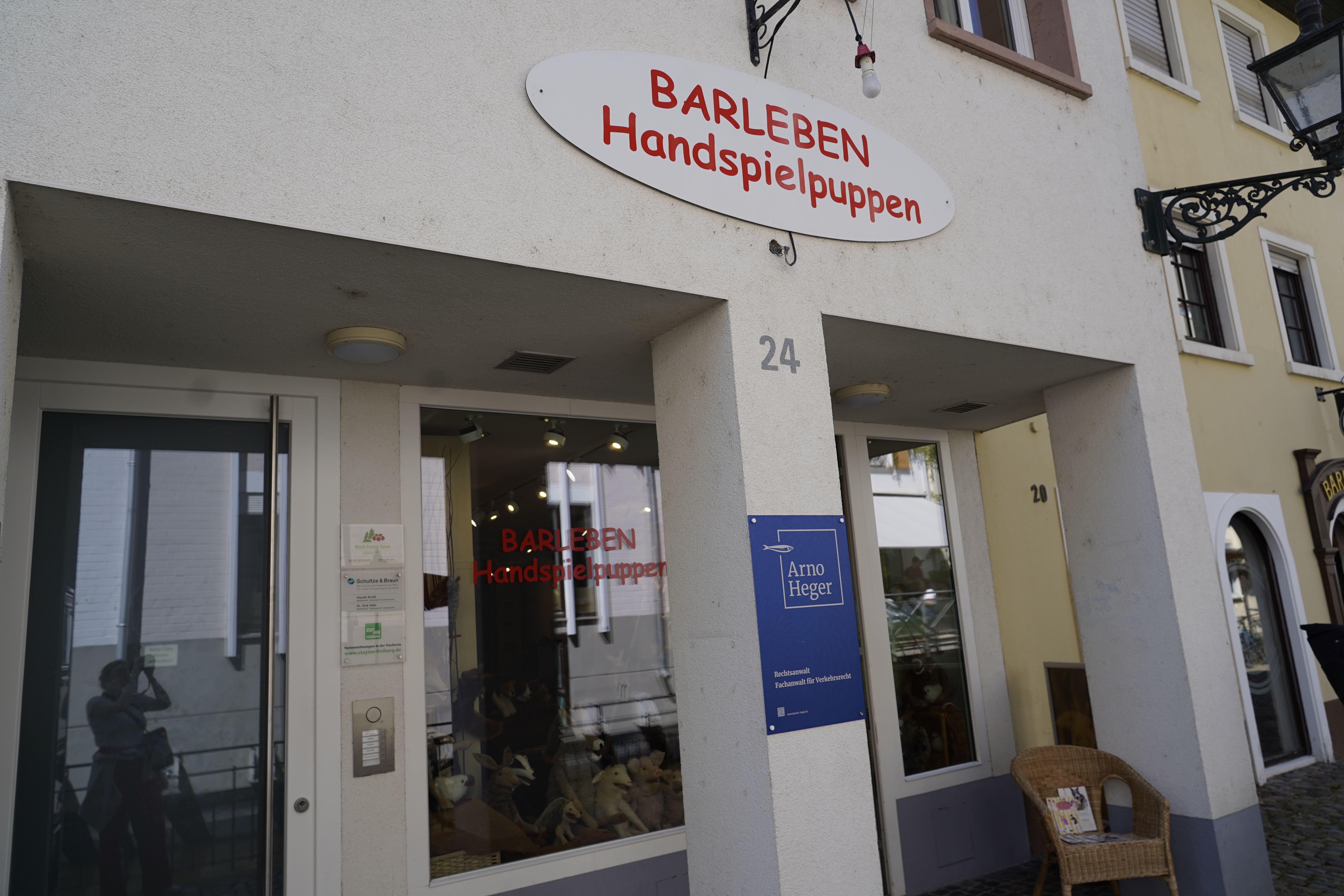 Eingang eines Geschäfts mit dem Schild 'Barleben Handspielpuppen'. Ein Korbstuhl steht vor der Tür.