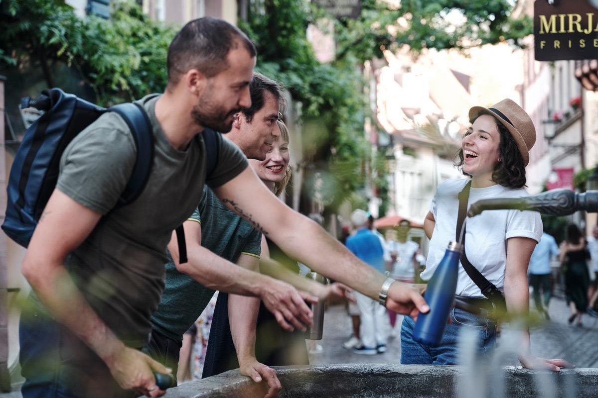 Eine Gruppe steht an einem Brunnen. Einer füllt eine Flasche auf 