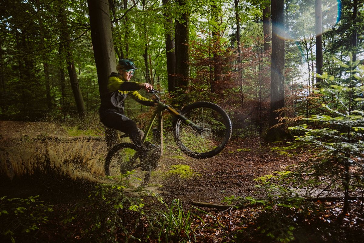 Mann macht ein Wheelie mit dem Mountainbike auf dem Trail im Wald 