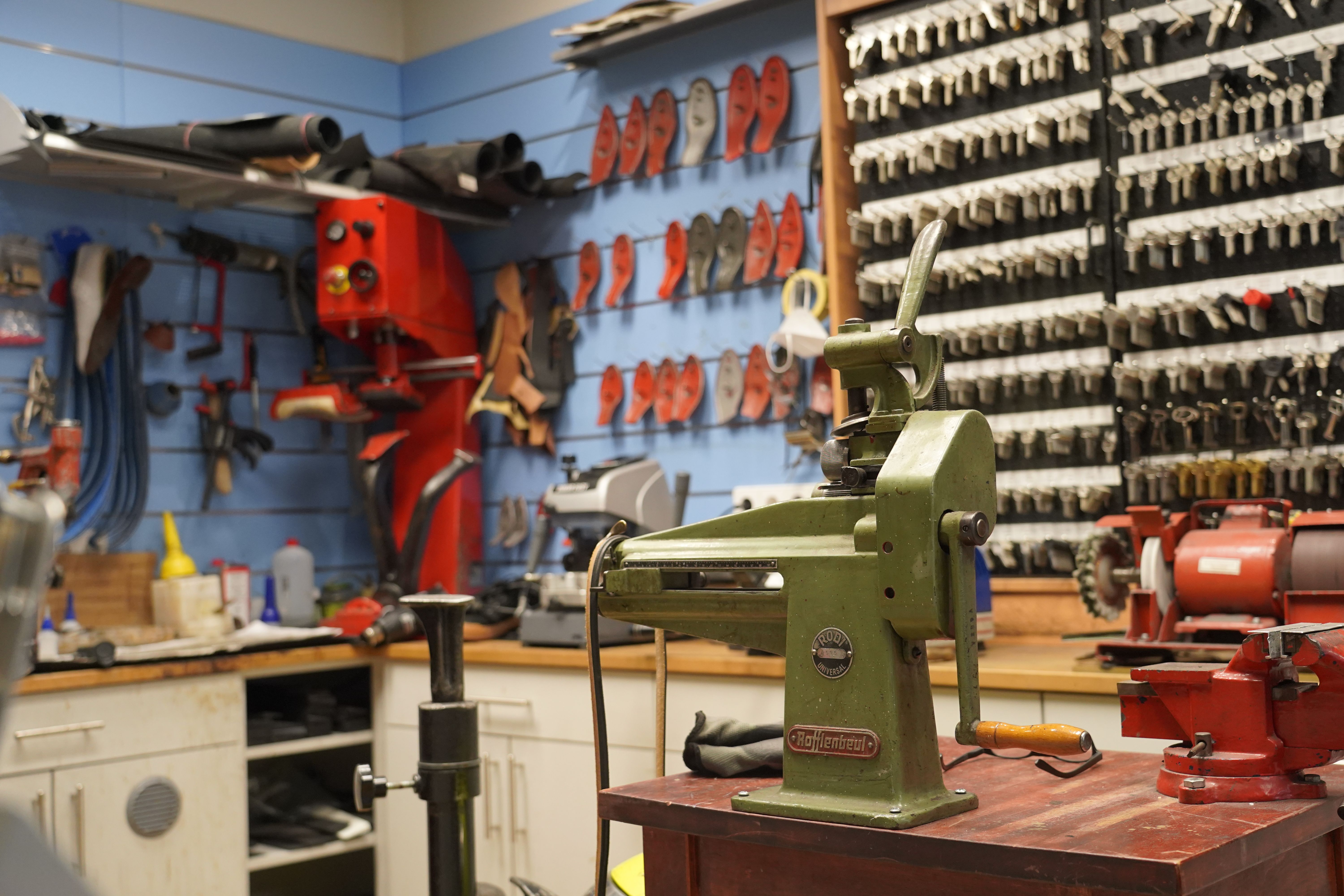 Werkstatt mit Schlüsselbrett, Maschinen und Werkzeugen. Eine grüne Maschine steht im Vordergrund, umgeben von Schlüsseln und Arbeitsgeräten.