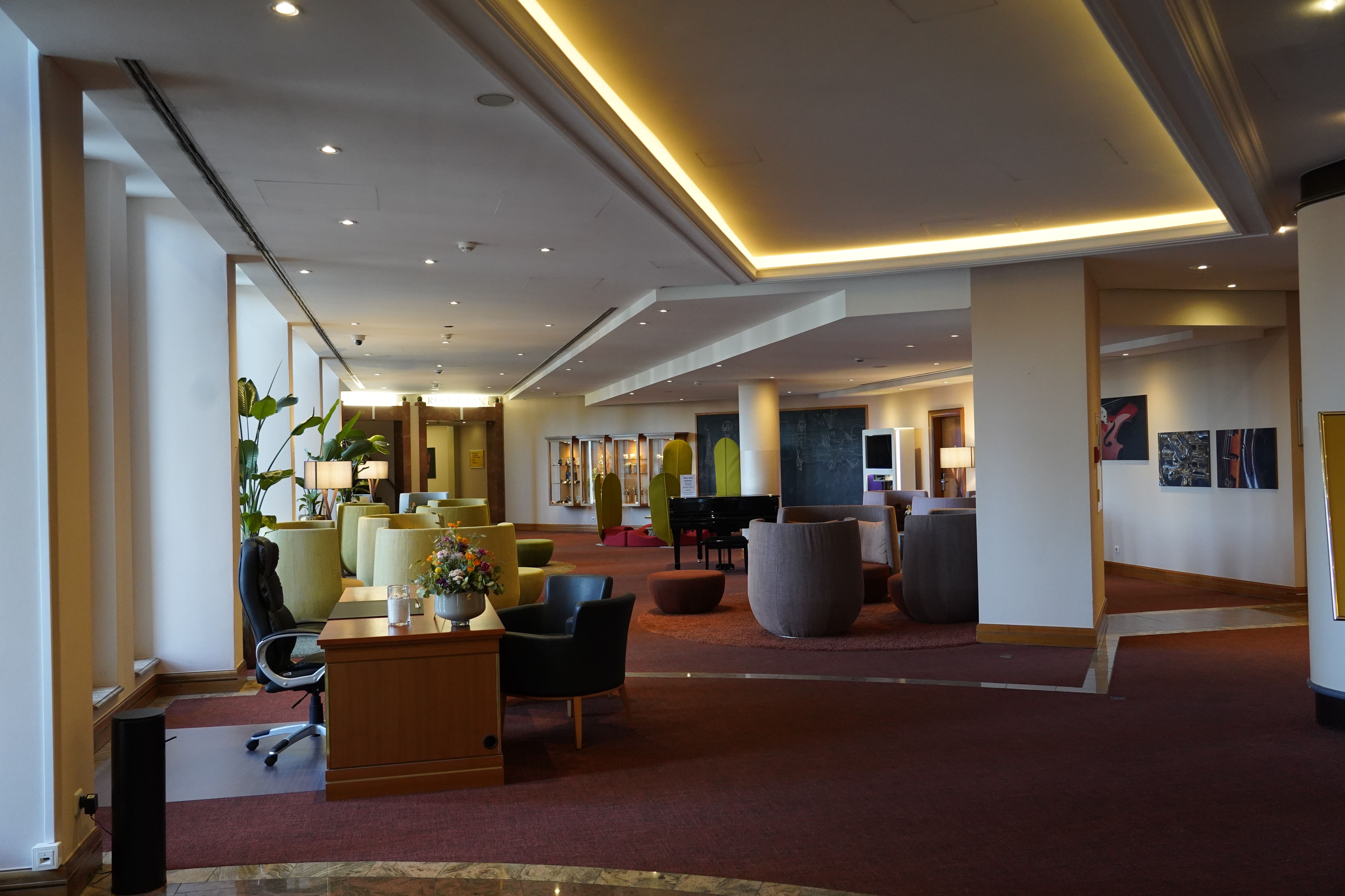 Moderne Hotel-Lobby mit gemütlichen Sitzbereichen, Pflanzen und einem Klavier. Warme Beleuchtung und stilvolle Dekoration schaffen eine einladende Atmosphäre.