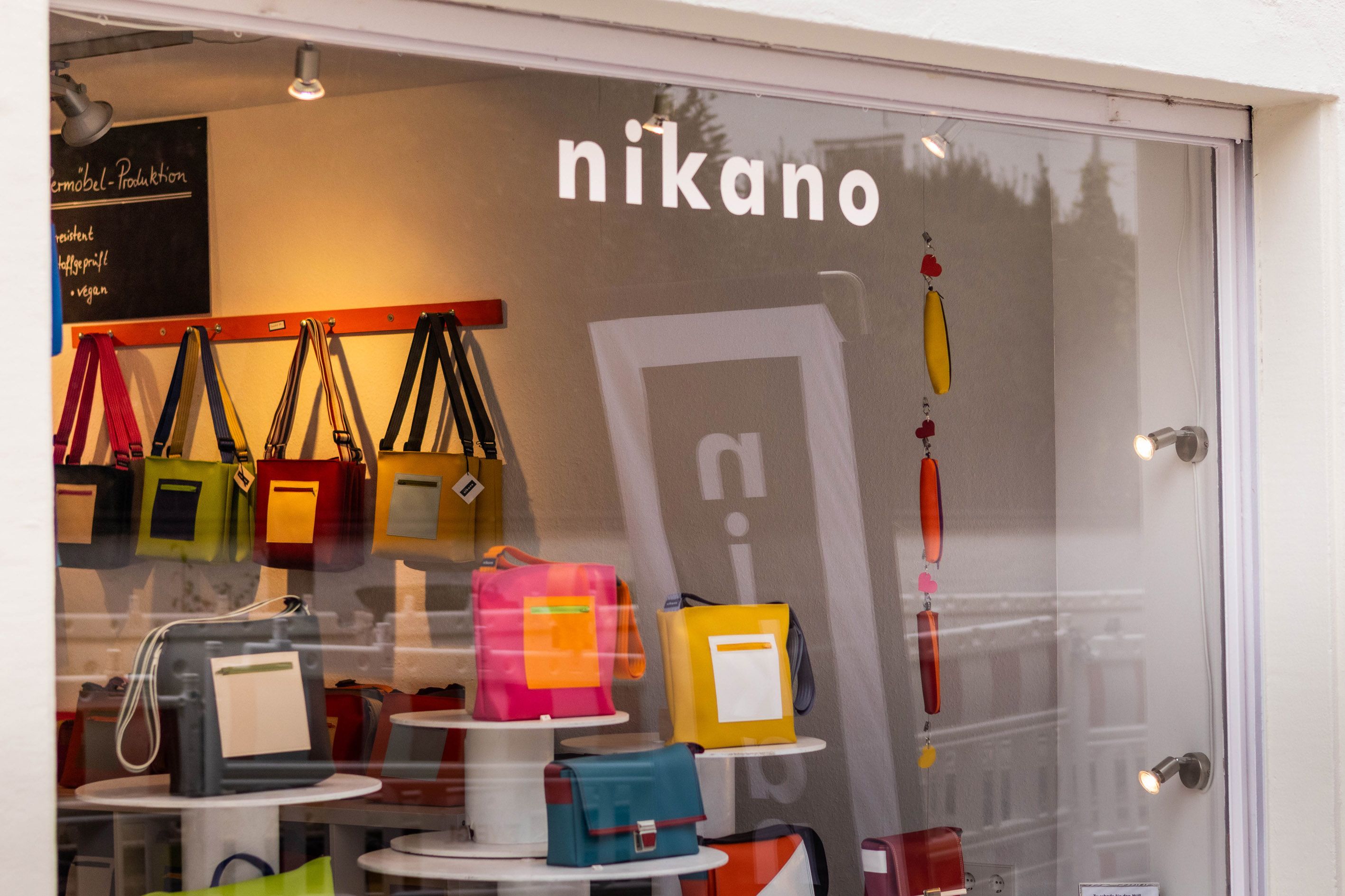 Ein Schaufenster mit bunten Taschen und dem Schriftzug 'nikano'. Die Taschen sind in verschiedenen Farben ausgestellt.