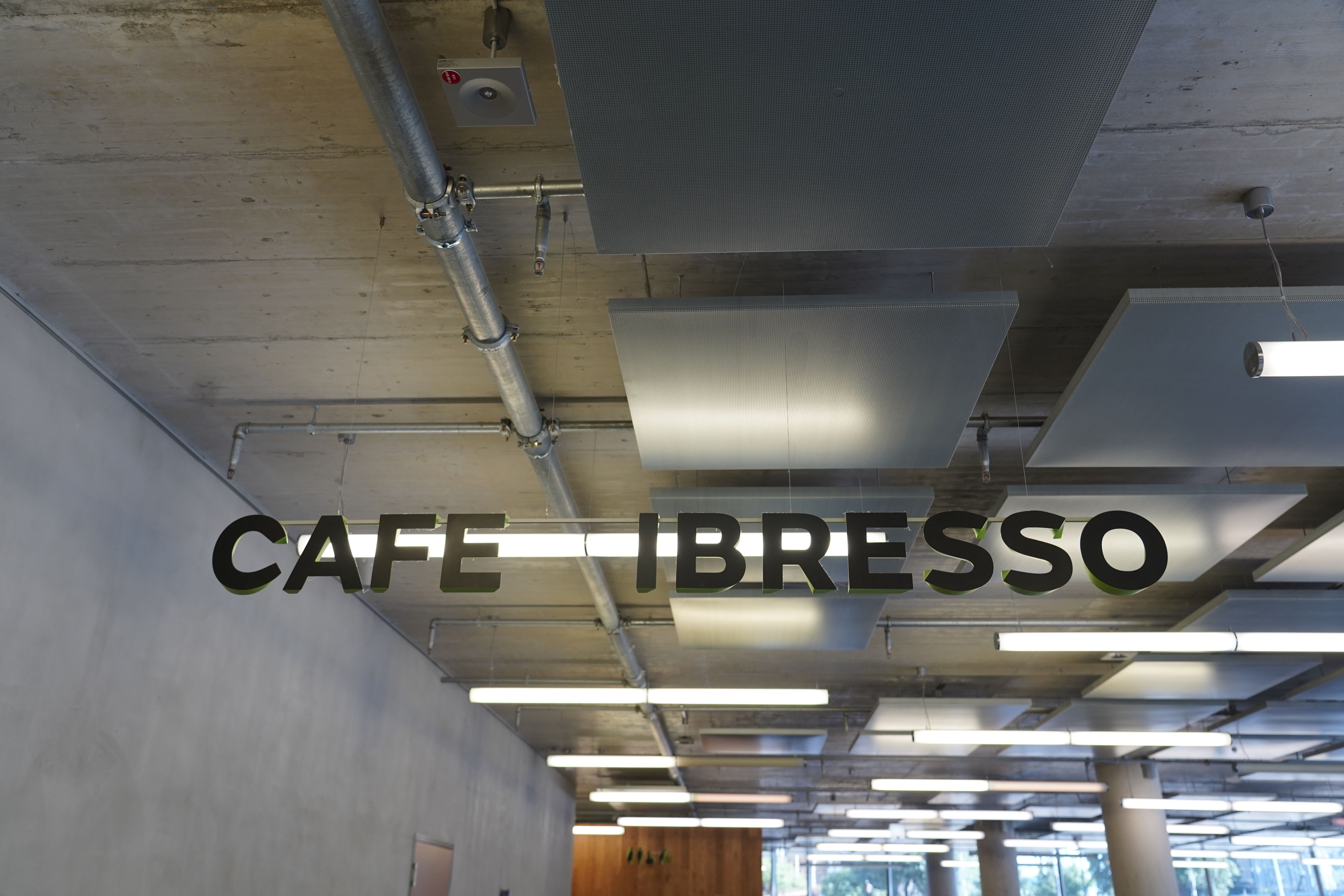 Schriftzug 'CAFE LIBRESSO' hängt von der Decke in einem modernen Café mit Betonoptik und Leuchtstoffröhren.