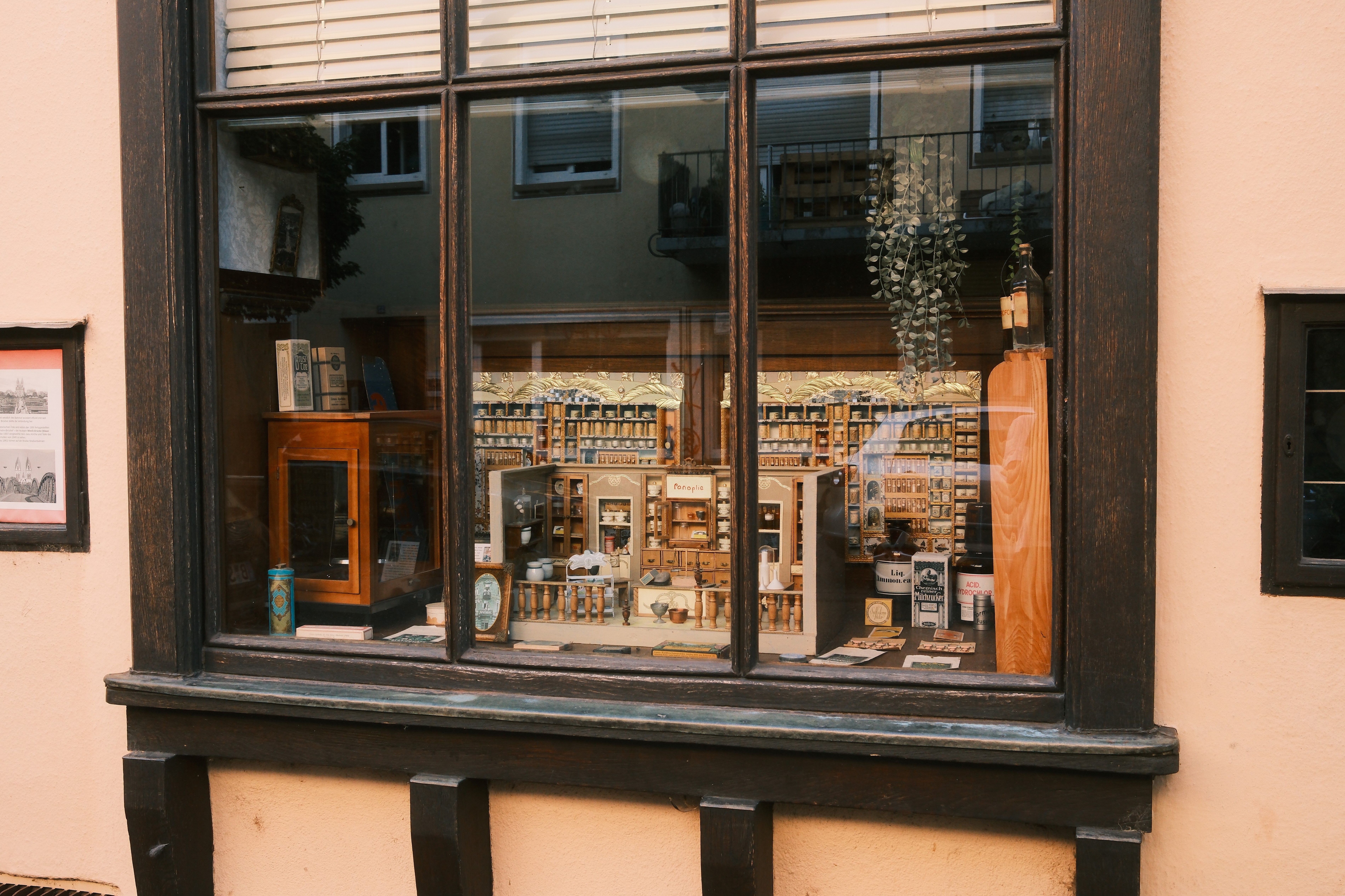 Ein Schaufenster zeigt eine historische Apotheke mit antiken Regalen, Flaschen und Dekorationen. Die Einrichtung wirkt nostalgisch und gut erhalten.