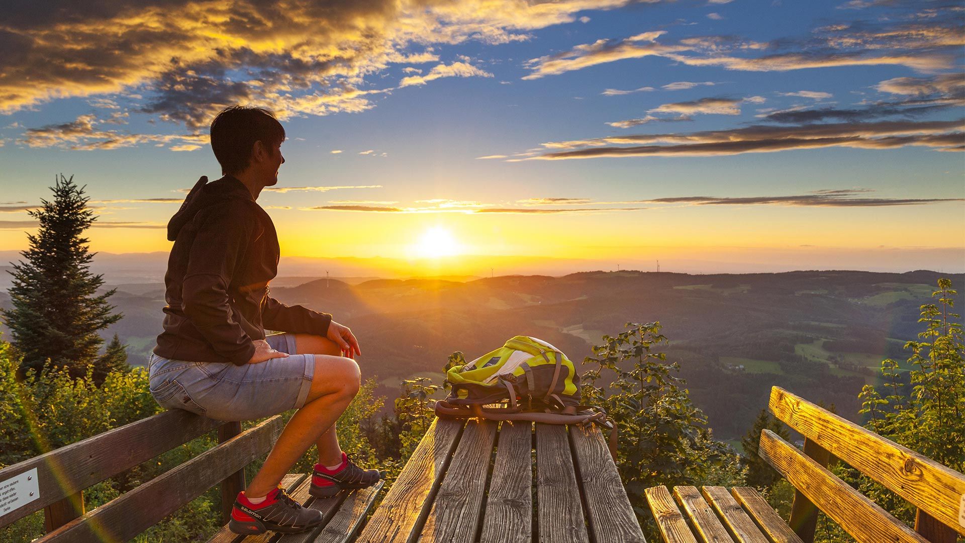 Schwarzwald Hörnleberg Sonnenuntergang. Eine Frau in Wanderkleidung sitzt auf der Rückenlehne einer Bank
