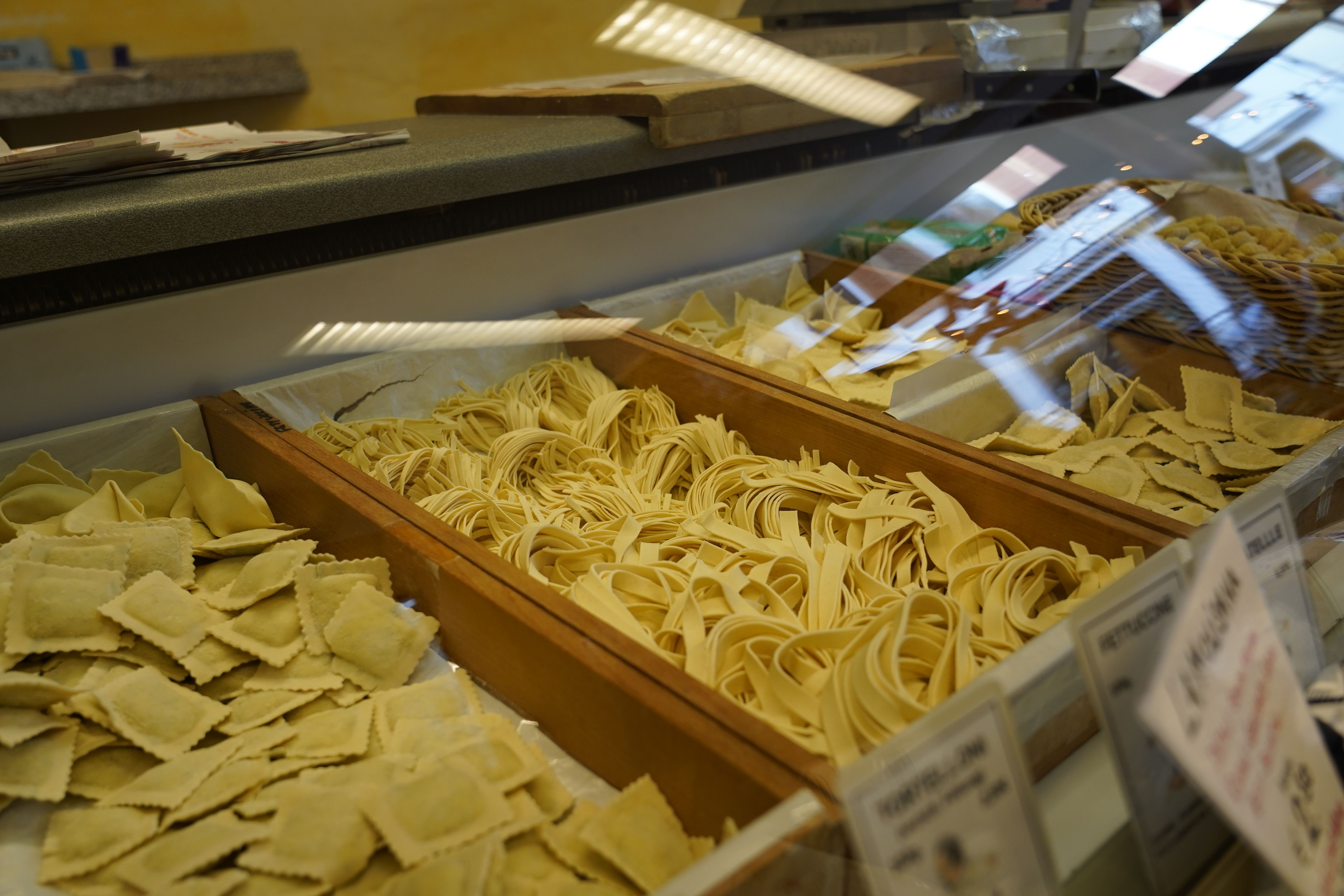Frische Pasta in einer Vitrine, darunter Ravioli und Tagliatelle. Die Nudeln sind in Holzfächern präsentiert.