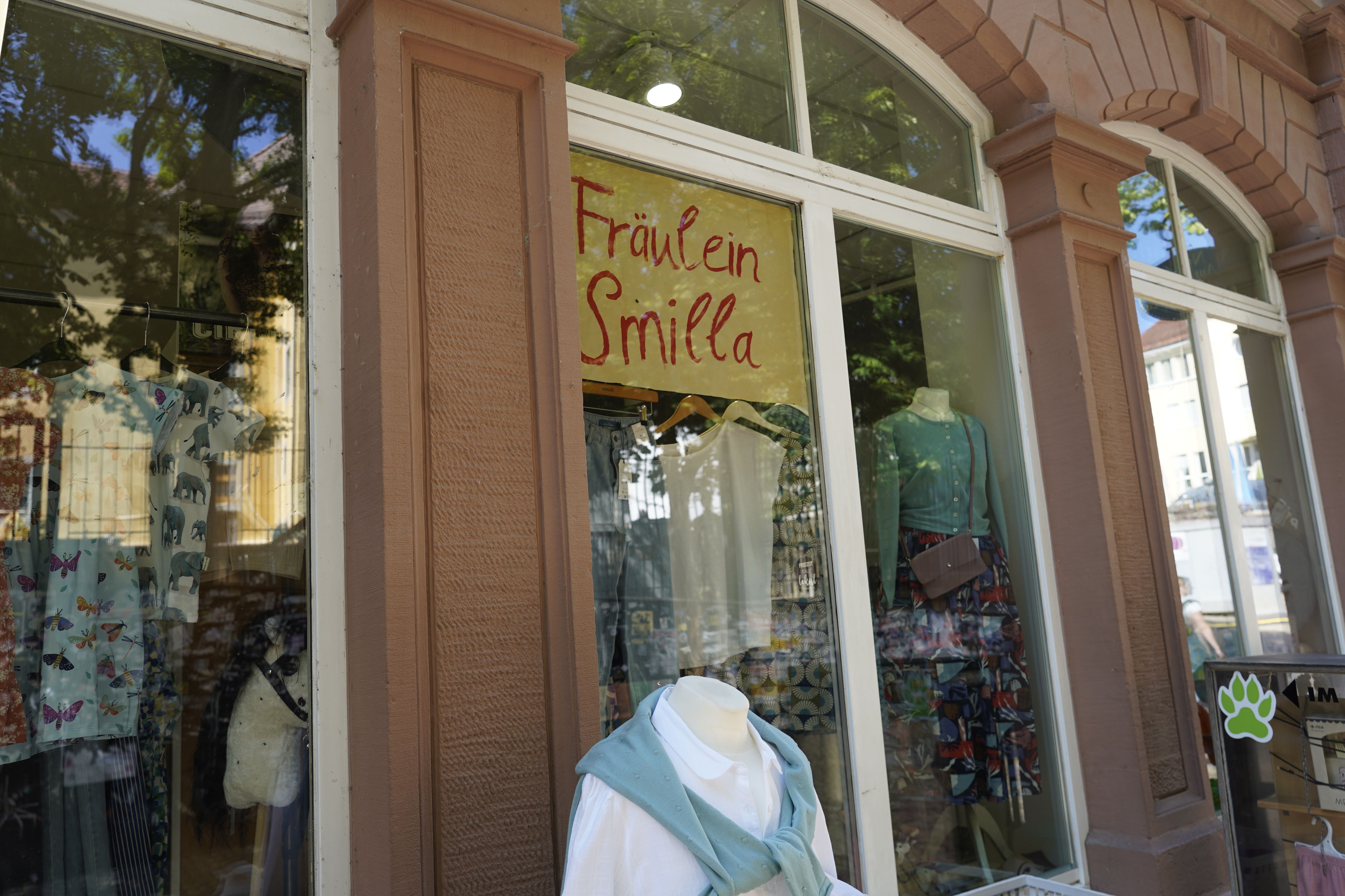 Schaufenster von 'Fräulein Smilla' mit Kleidungsauslage. Mannequins tragen bunte Outfits. Geschäft in einem Gebäude mit großen Fenstern.