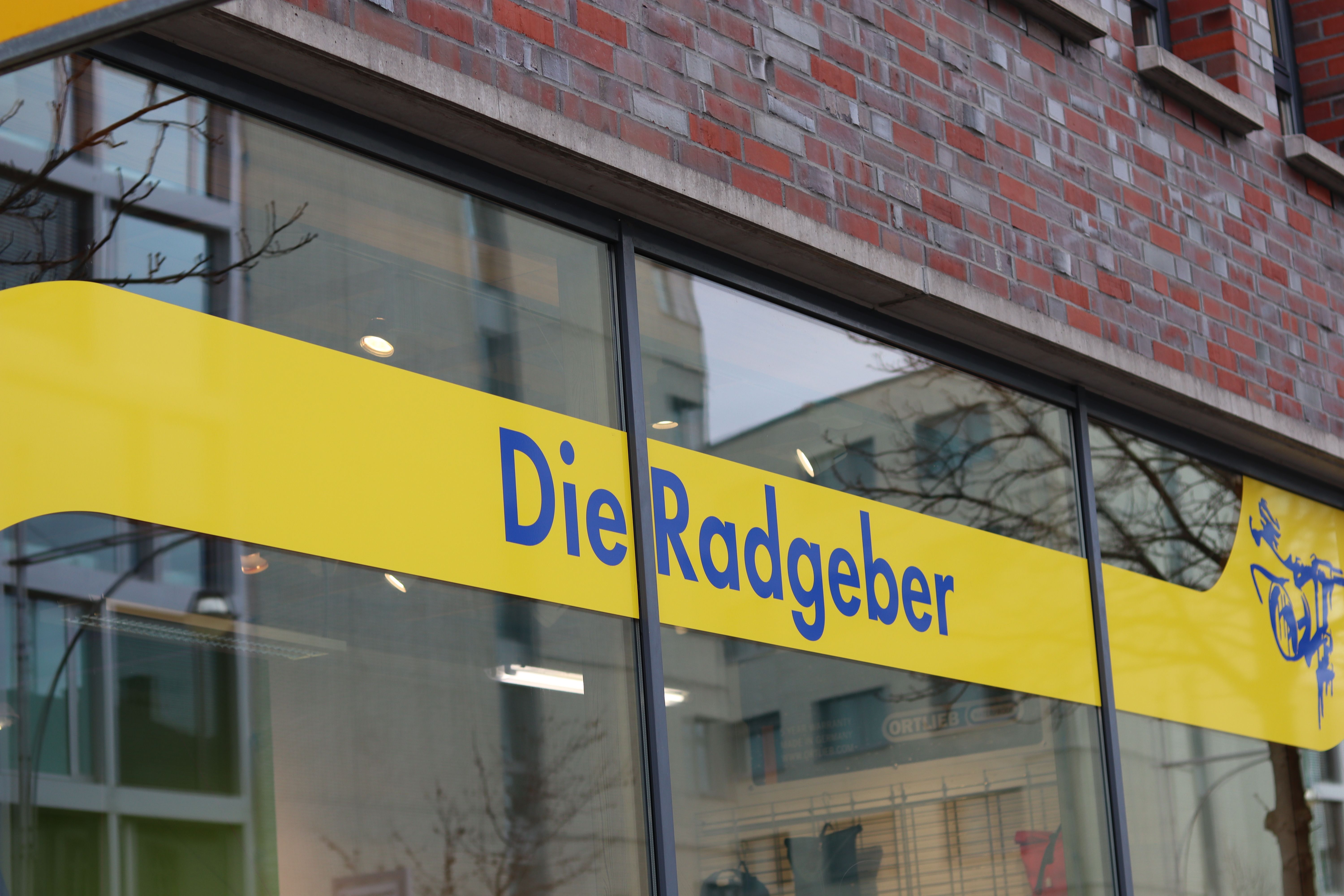 Schaufenster eines Geschäfts mit gelbem Schild und blauer Aufschrift 'Die Radgeber'. 