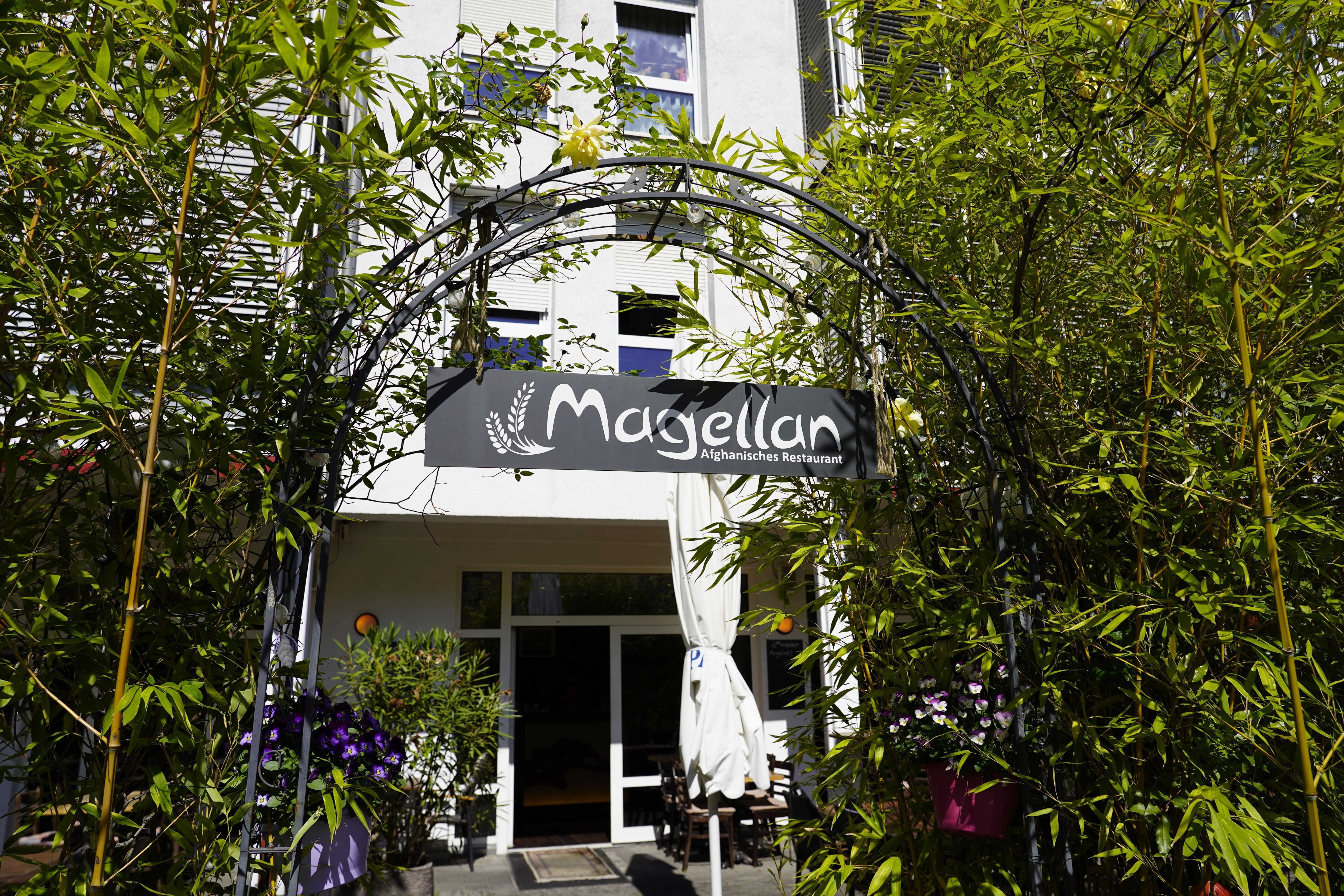 Eingang des Magellan afghanischen Restaurants, umgeben von grünen Pflanzen und einem dekorativen Schildbogen.