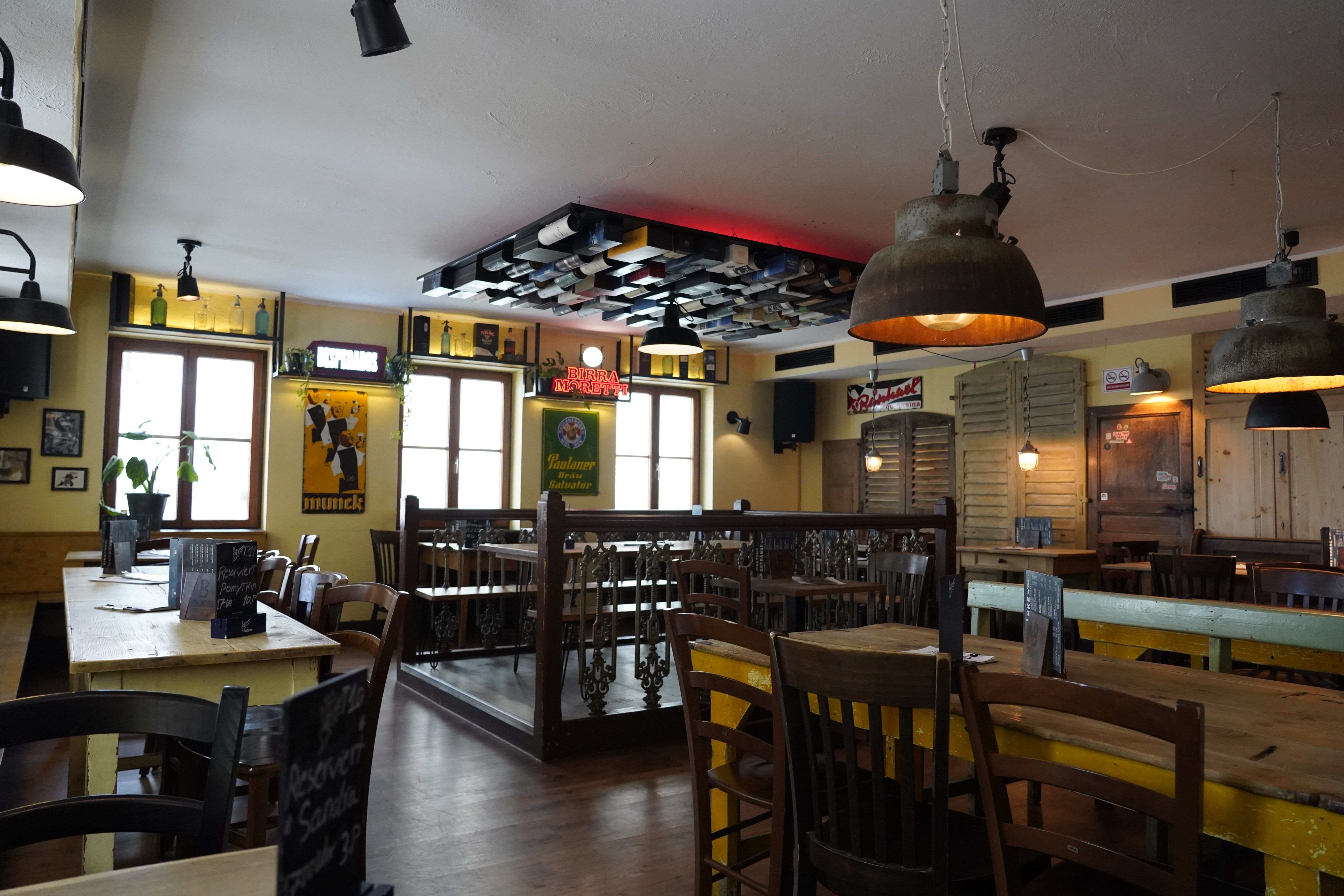 Rustikales Restaurant mit Holztischen, Stühlen, alten Schildern und Flaschen als Dekoration. Gemütliche Atmosphäre mit warmem Licht.