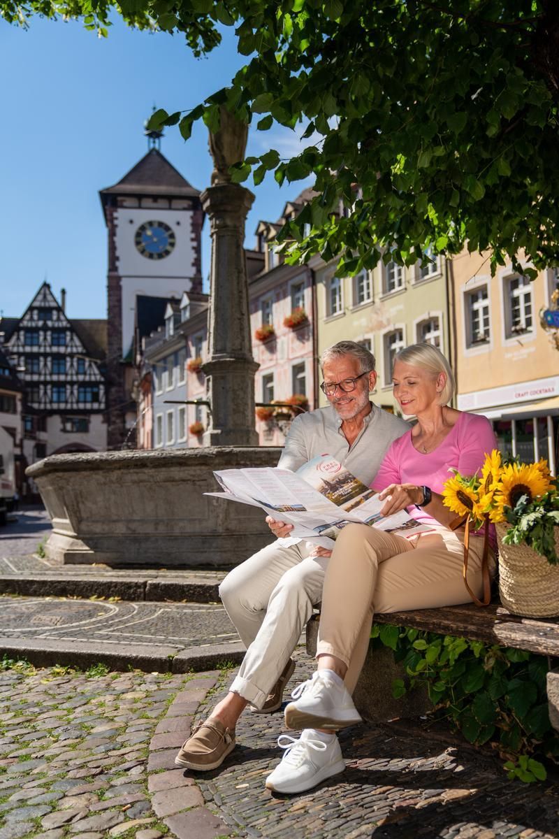 Ein Paar Sitzt unter der Linde am Oberlindenbrunnen und schaut sich einen Stadtplan an