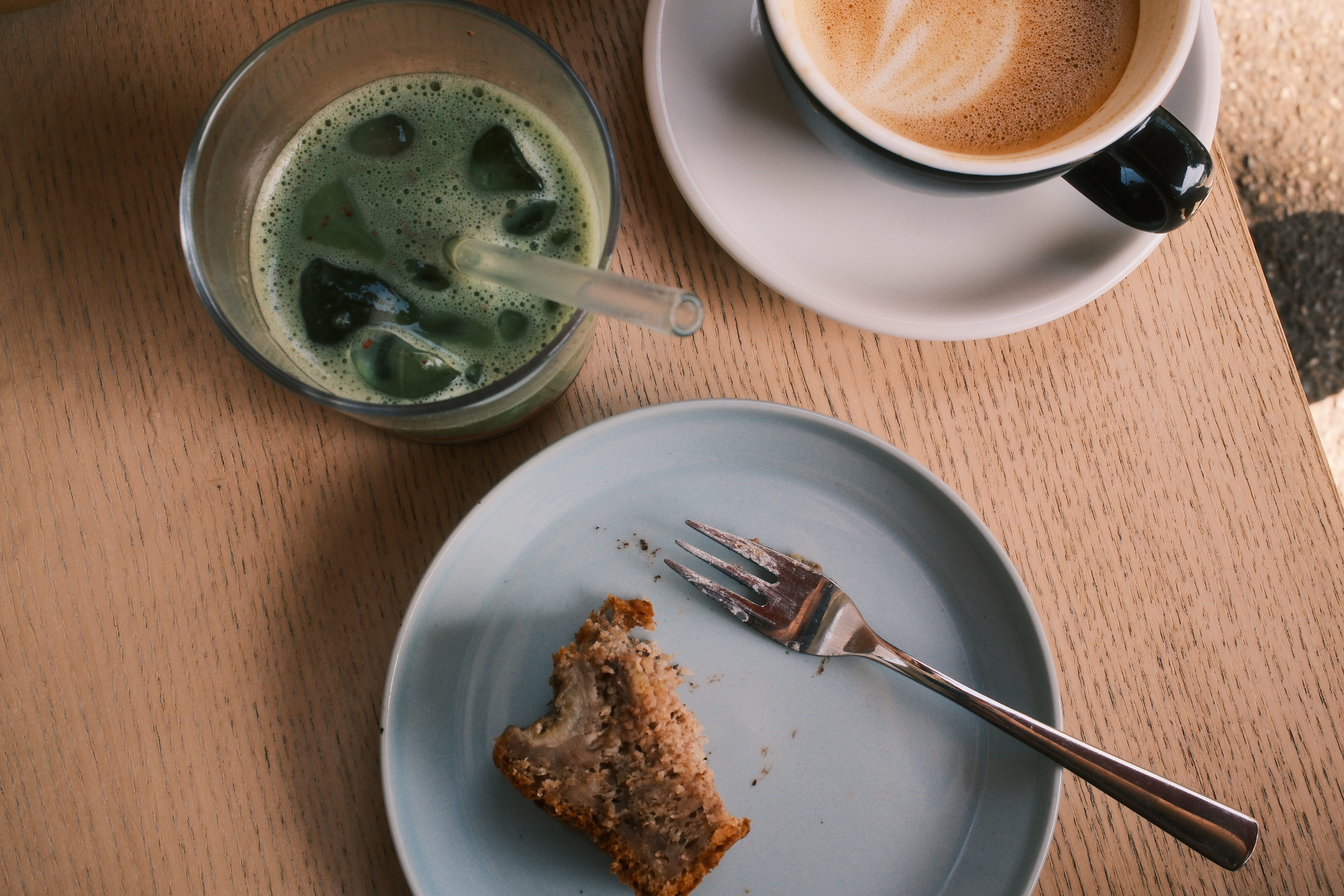 Kohi-Café-Copyright-FWTM-Heinzler: Café-Tisch mit grünem Getränk, Espresso, Teller und angebissenem Kuchen von oben.