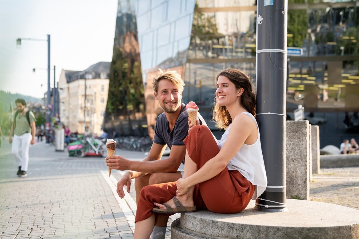 Eine Frau und ein Mann sitzen vor der Uni Bibliothek und essen Eis 