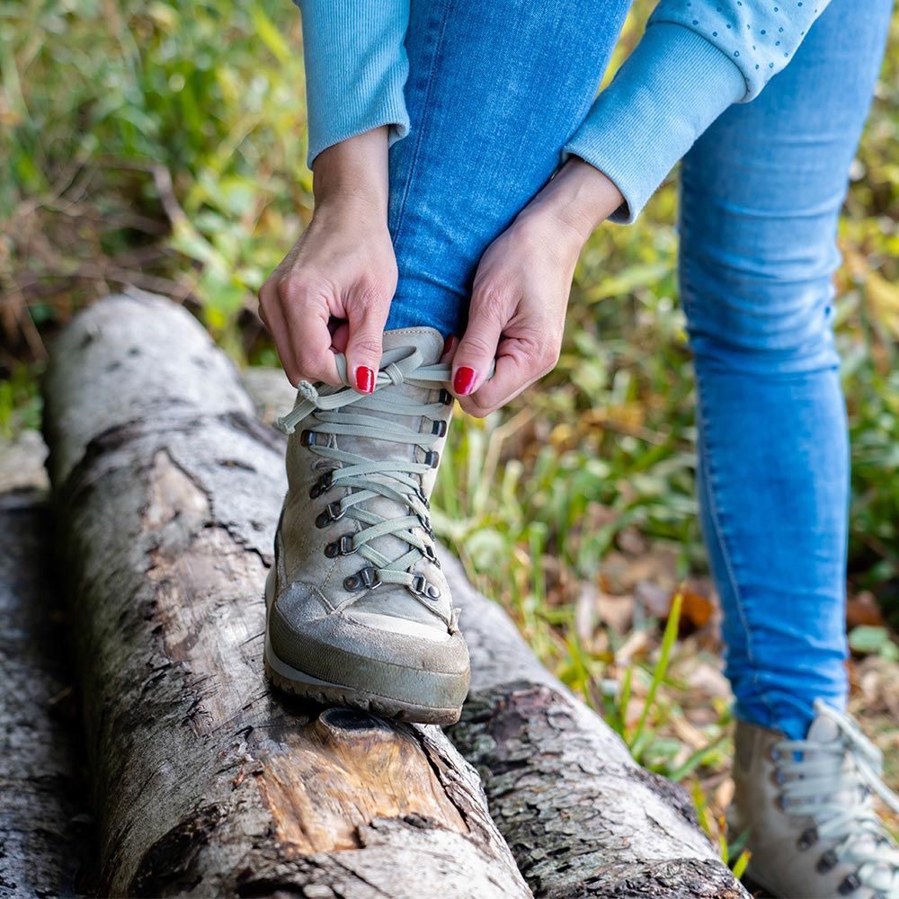 Nahaufnahme wie sich eine Frau die Wanderschuhe auf einem Baumstamm zuschnürt