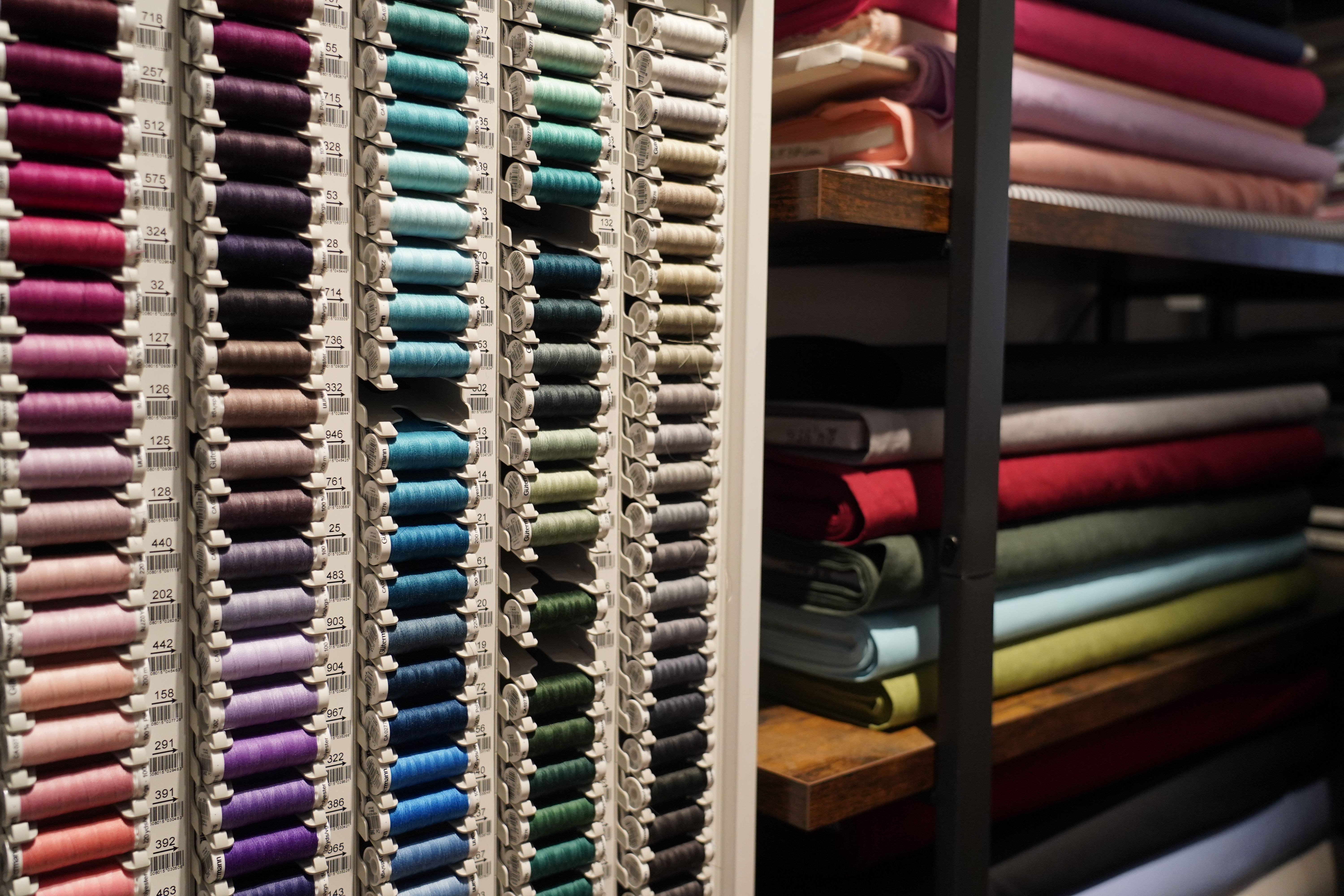 Regale mit bunten Garnrollen und Stoffen in verschiedenen Farben in einem Nähgeschäft.