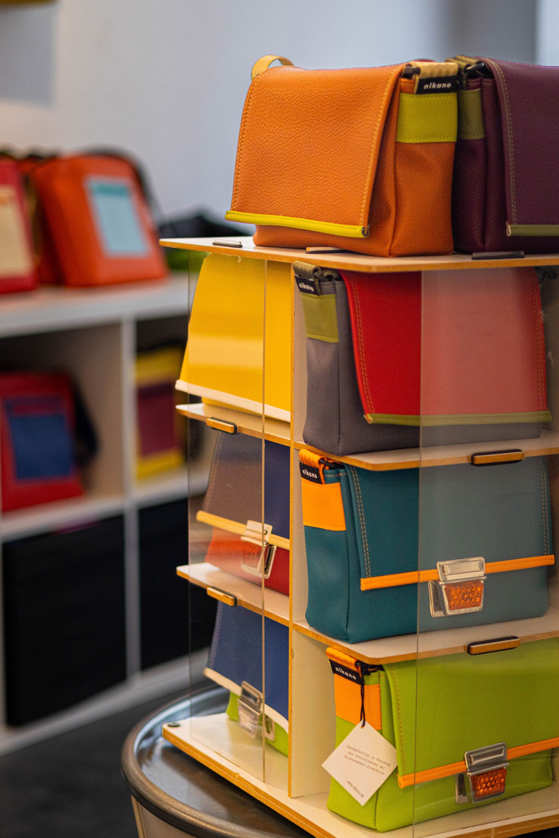 Verschiedene bunte Taschen sind in einem Regal ausgestellt. Die Taschen haben leuchtende Farben wie Orange, Blau und Grün.