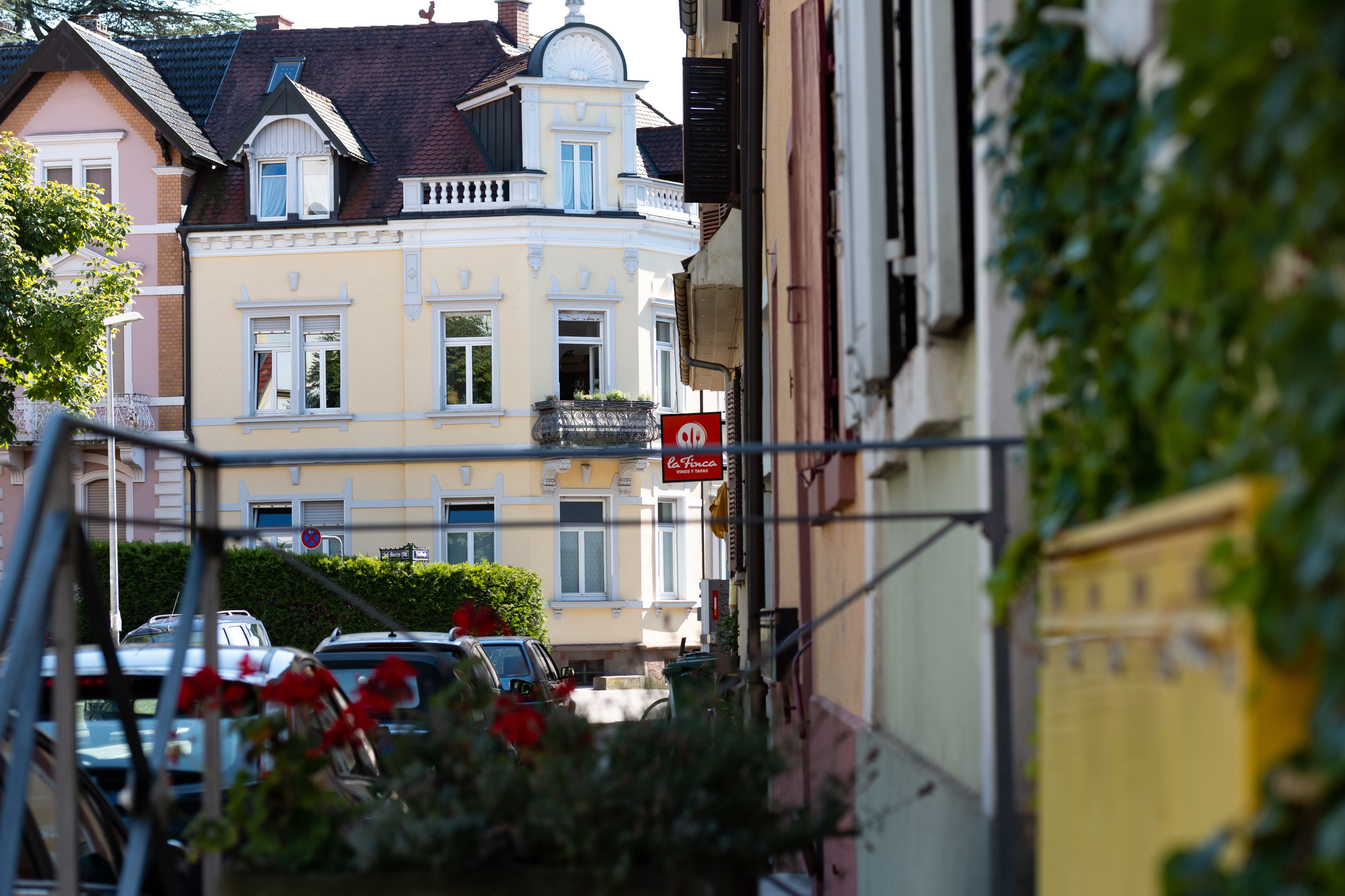 Blick auf eine Straße in Freiburg-Herdern mit historischen Gebäuden und parkenden Autos. Ein Schild mit der Aufschrift 'le Finca' ist sichtbar.