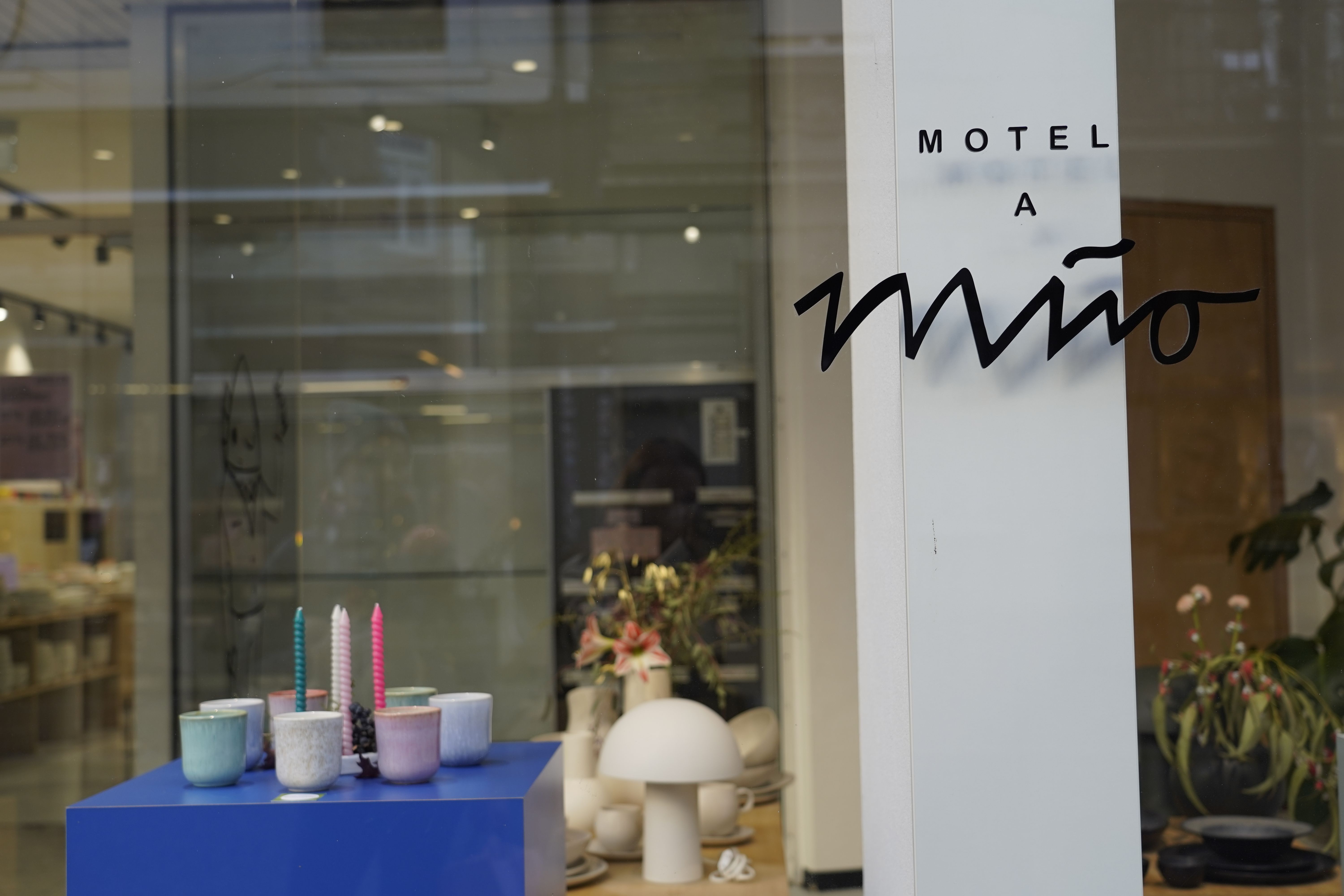 Schaufenster von Motel a Miio mit Kerzen und Keramik auf einem blauen Podest. Der Ladenname ist an der Scheibe angebracht.