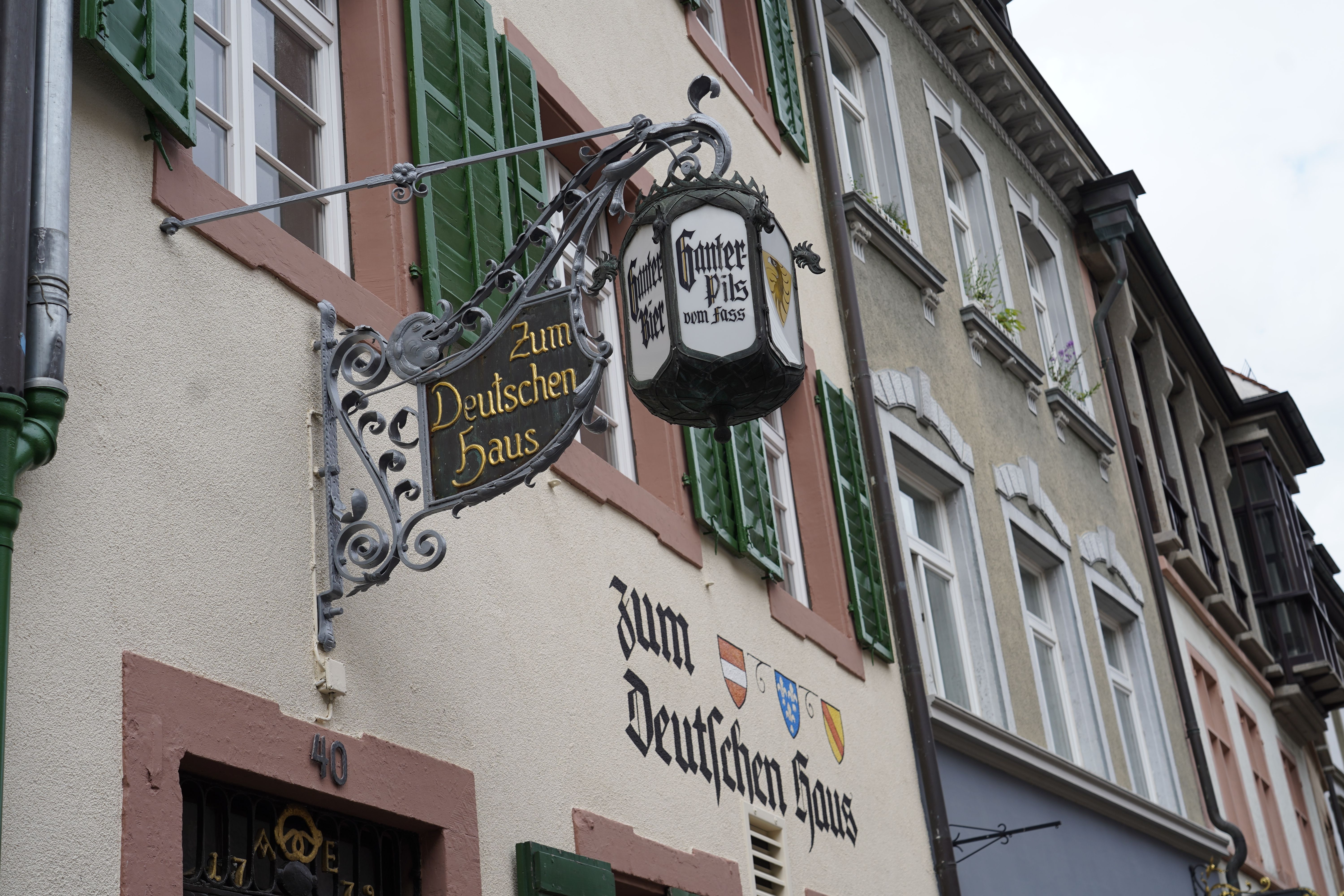 Traditionelles Gasthaus mit Schild 'Zum Deutschen Haus', grünen Fensterläden und Wappen an der Fassade.