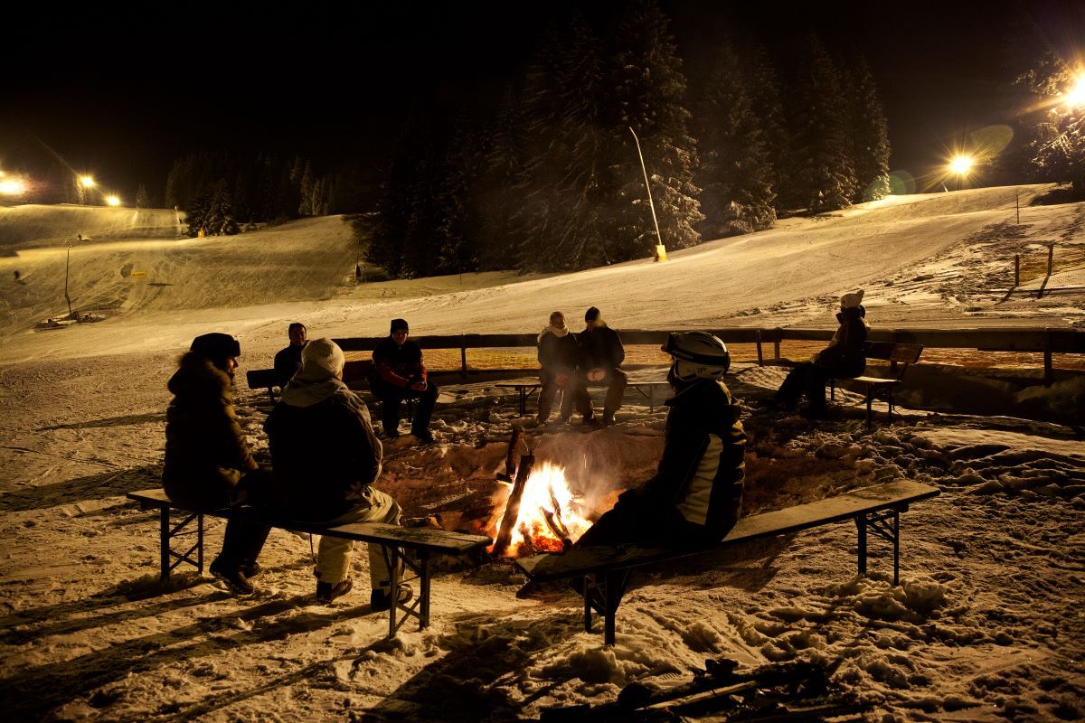 Personen sitzen um ein Feuer vor dem Skilift Haldenköpfle