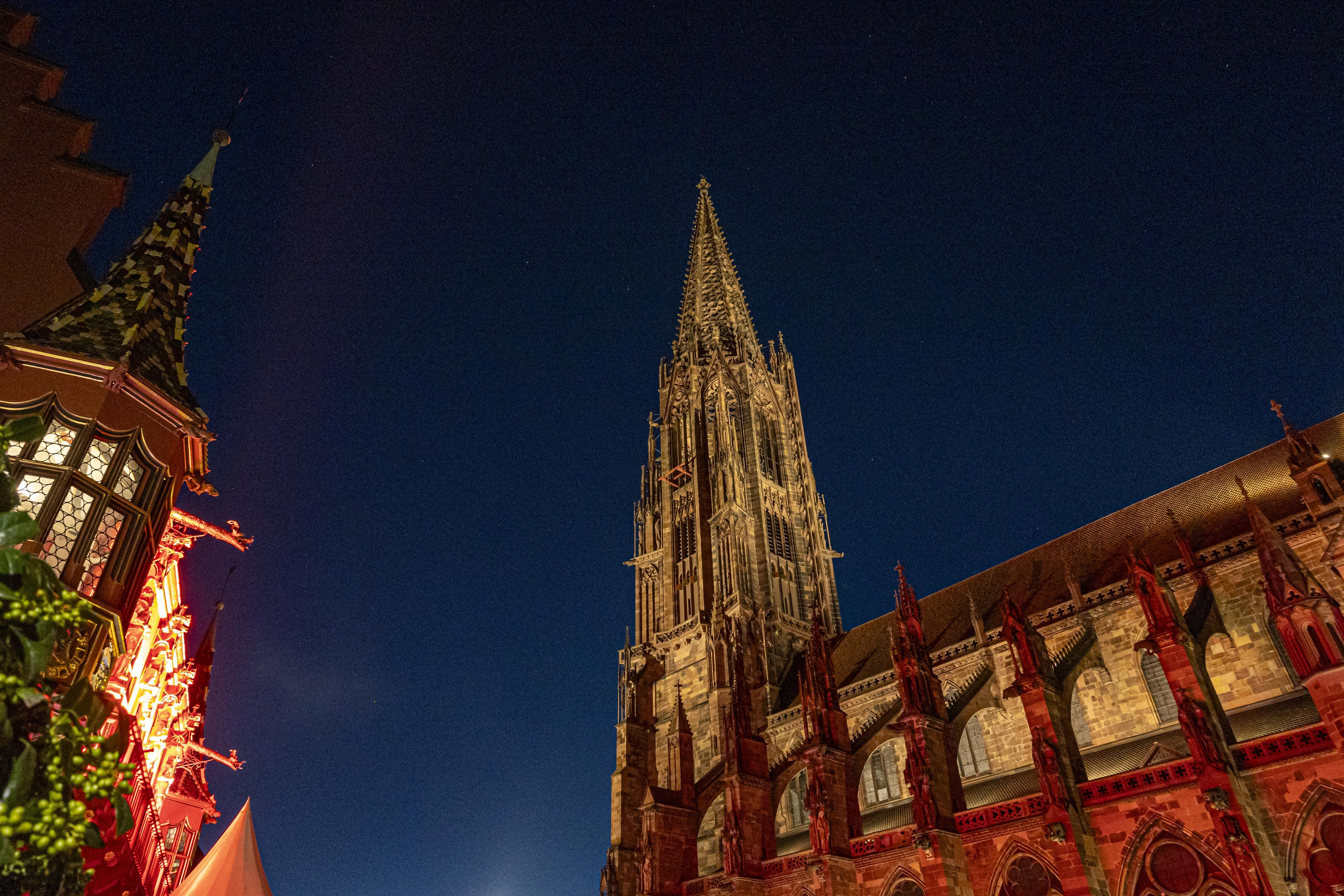 Das Freiburger Münster bei Nacht, der beleuchtete Turm ragt in den klaren Nachthimmel. 