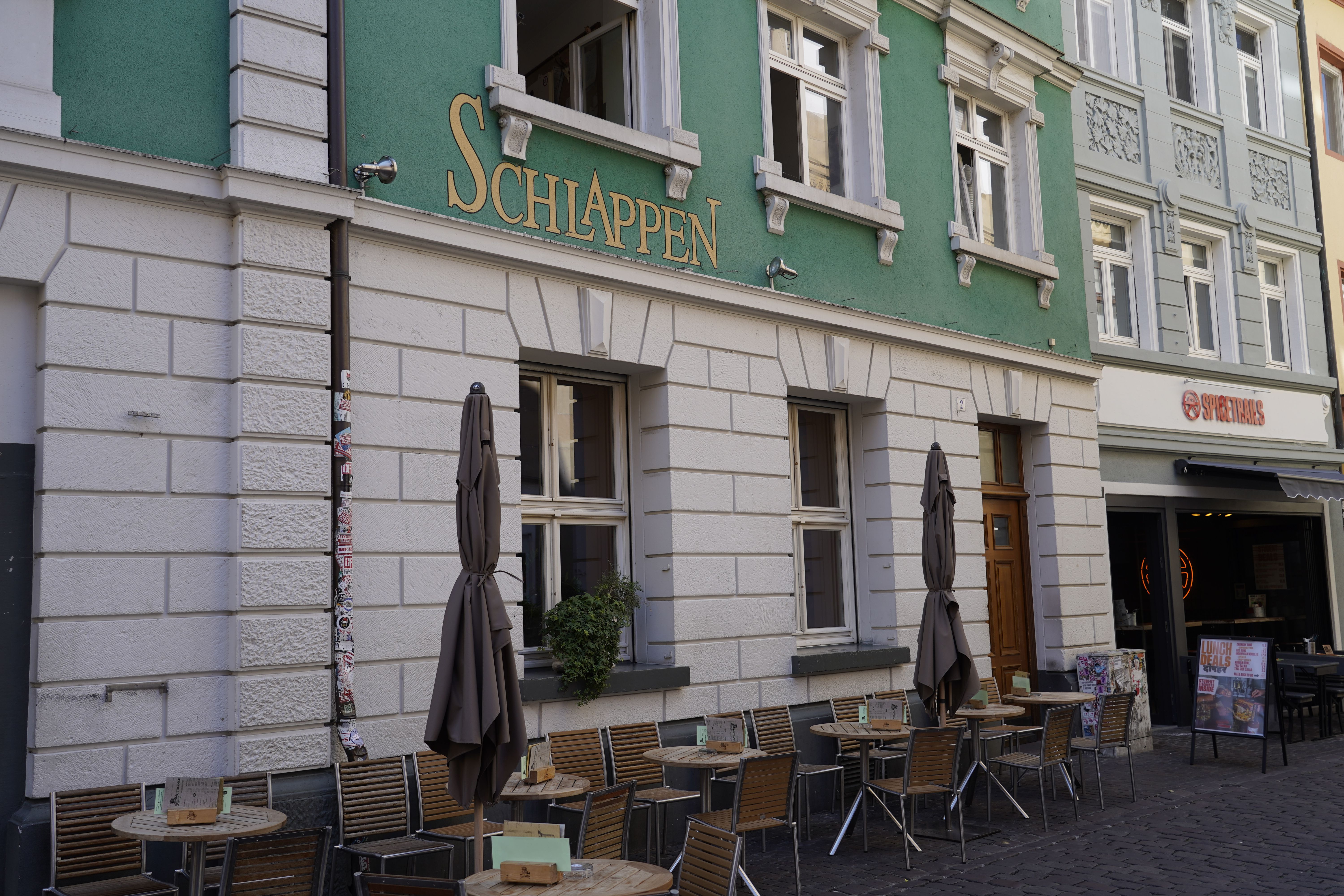 Außenansicht eines Cafés namens Schlappen in Freiburg. Vor dem Gebäude stehen Tische und Stühle auf dem Gehweg.