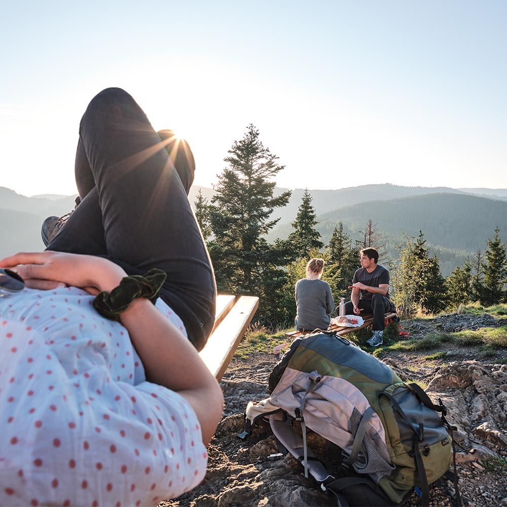 Wanderpause Schluchsee Schwarzwald eine Person liegt auf den Felsen und ruht sich aus, zwei Personen sitzen im Hintergrund und machen eine Vesperpause