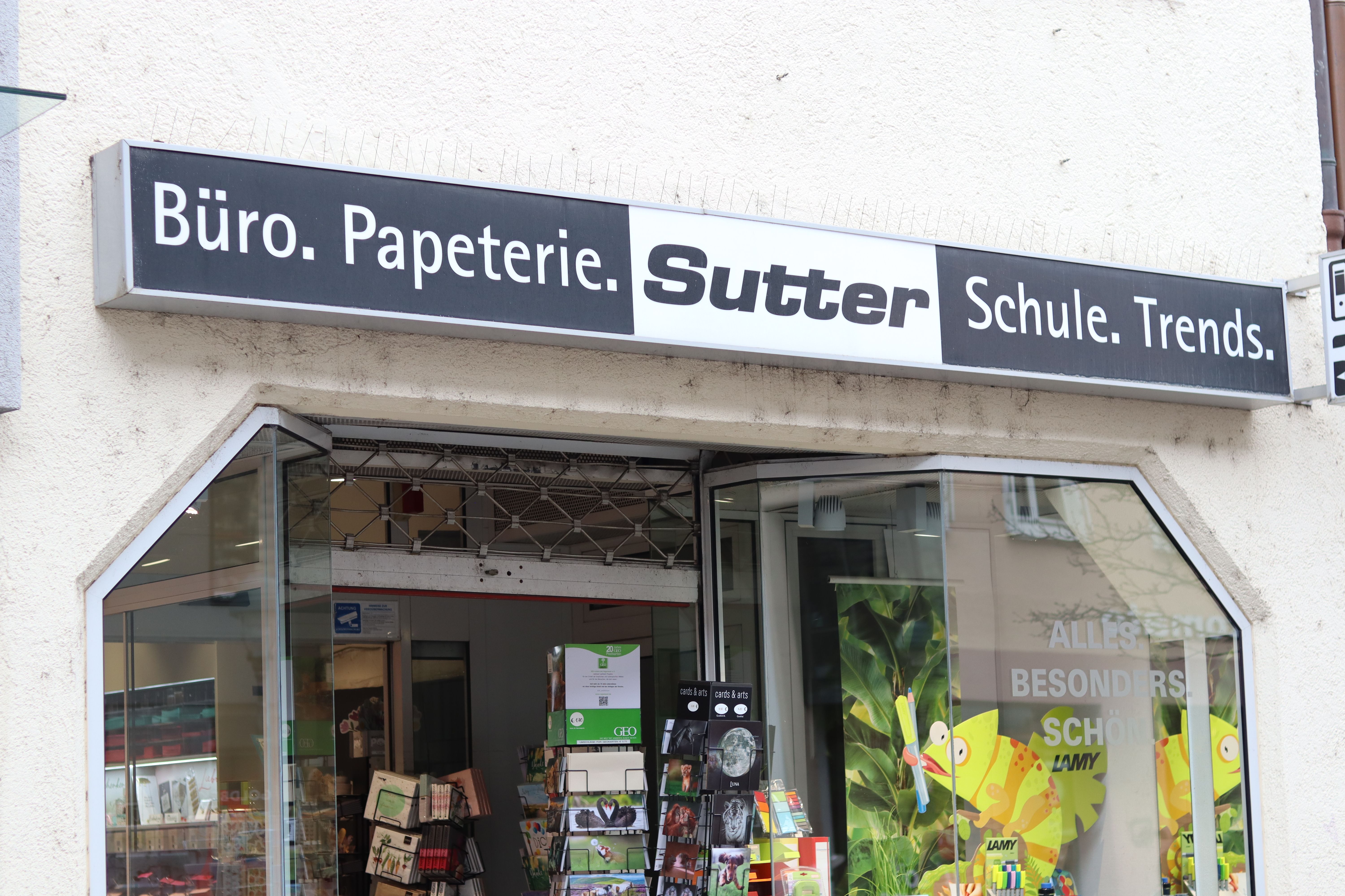 Eingang eines Schreibwarengeschäfts mit dem Schild 'Büro. Papeterie. Sutter Schule. Trends.' und einem Schaufenster mit bunten Produkten.