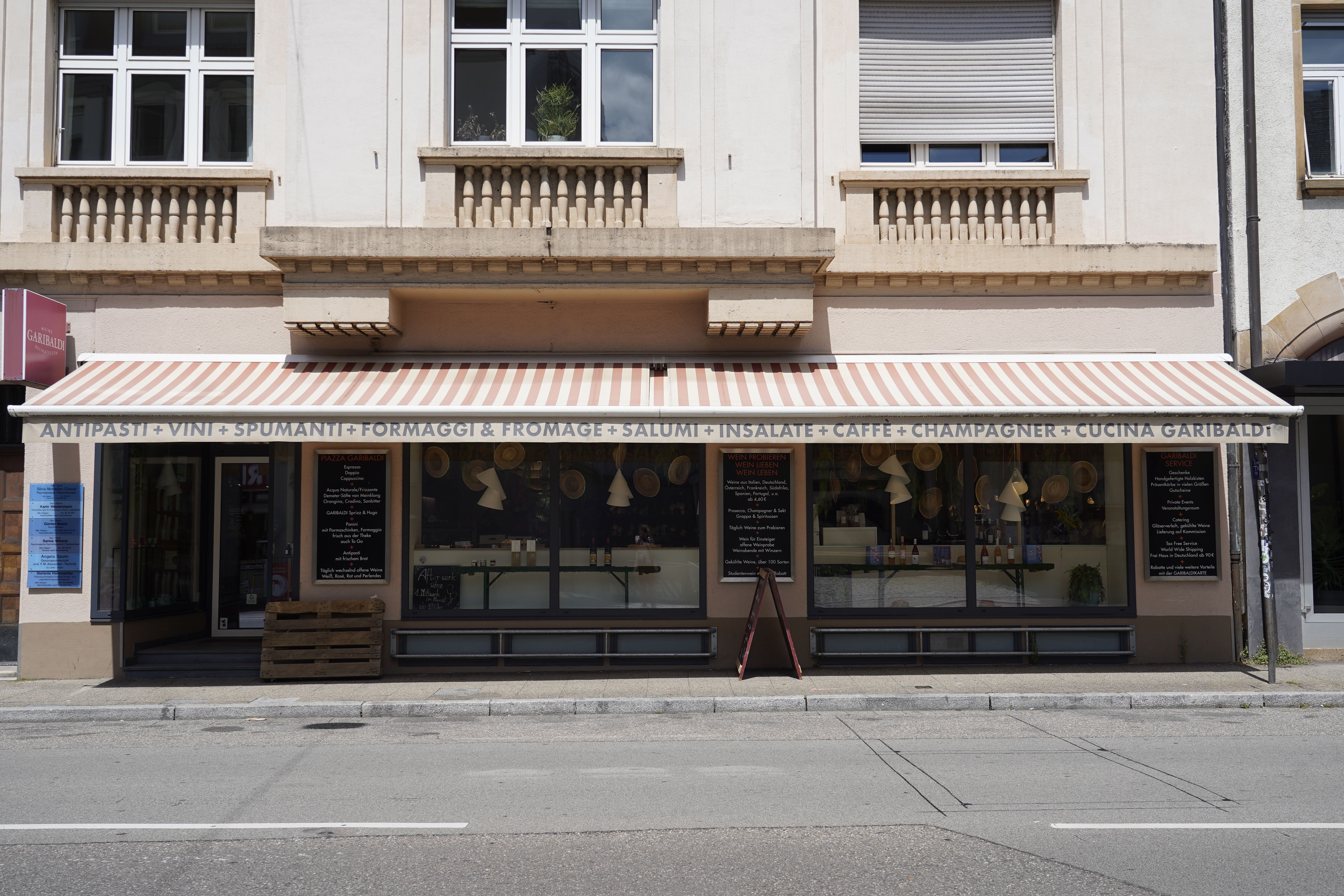 Italienischer Feinkostladen mit gestreifter Markise, Schaufenstern und Beschriftung für Antipasti, Vini, Formaggi und mehr.