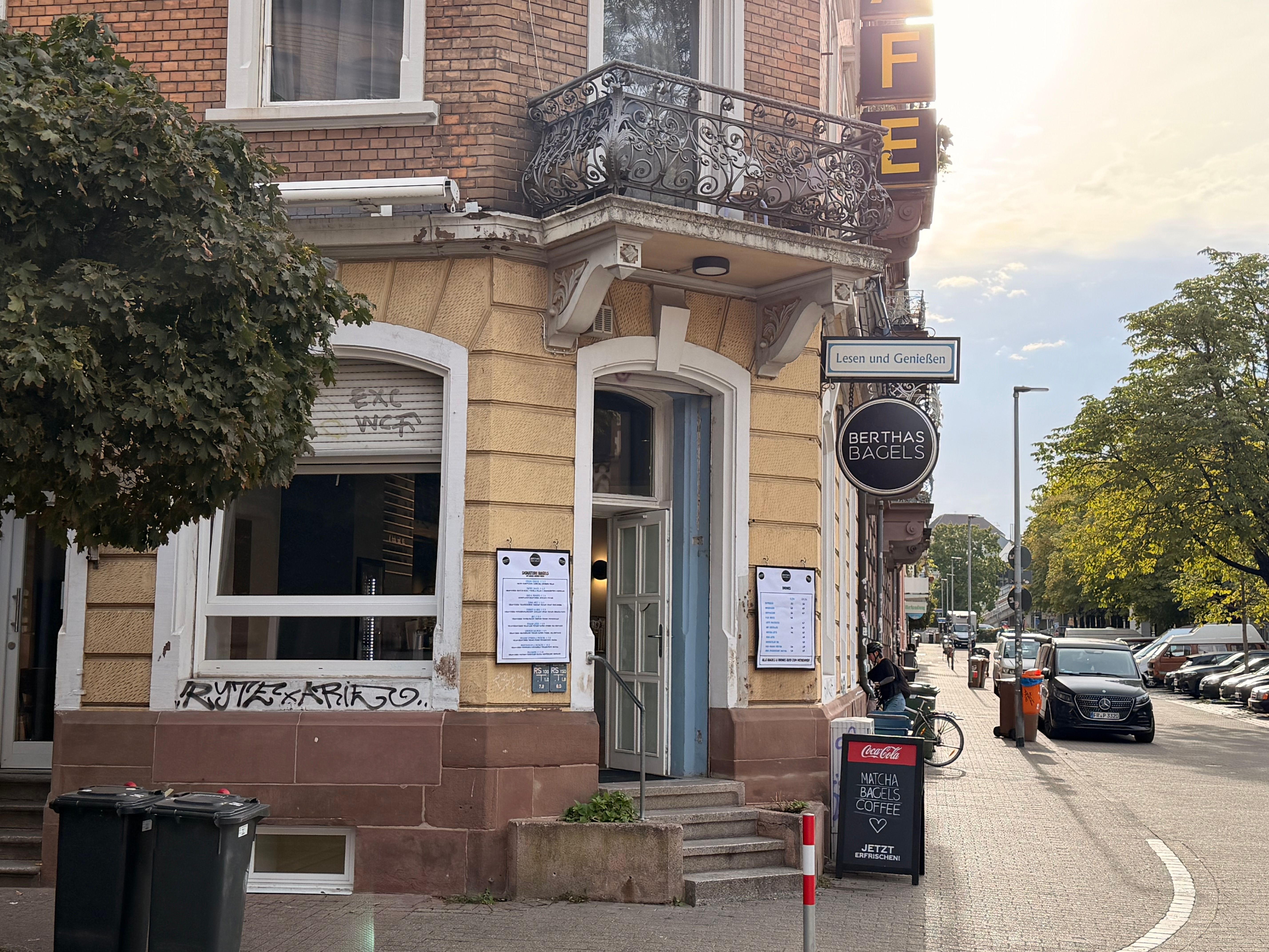 Altbau an der Straßenecke mit dem Café Berthas Bagels, Schildern und Balkon im Abendlicht.