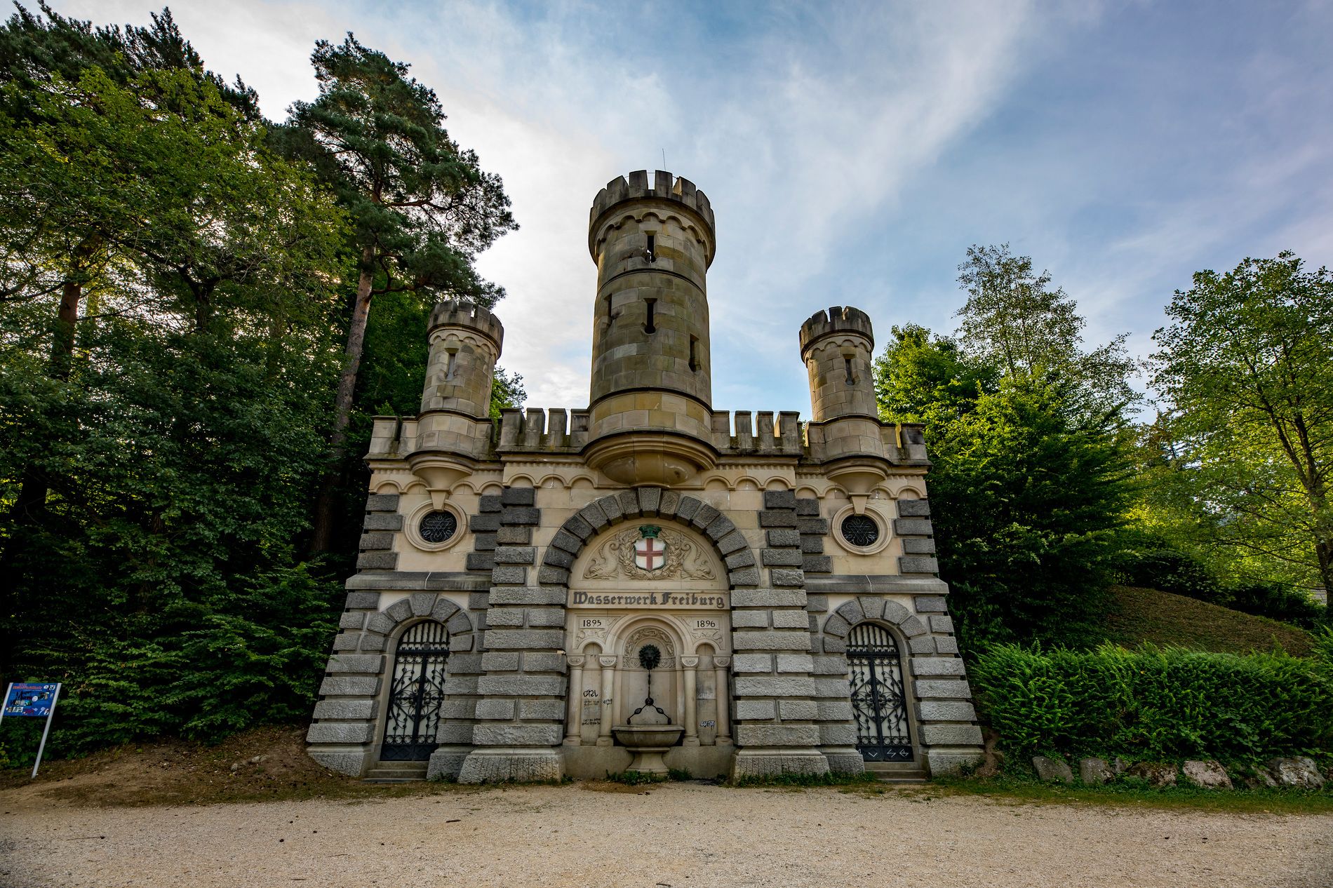 Das Wasserschlössle in Freiburg ist ein historisches Gebäude mit Türmen und Bögen, umgeben von üppigem Grün und Bäumen.
