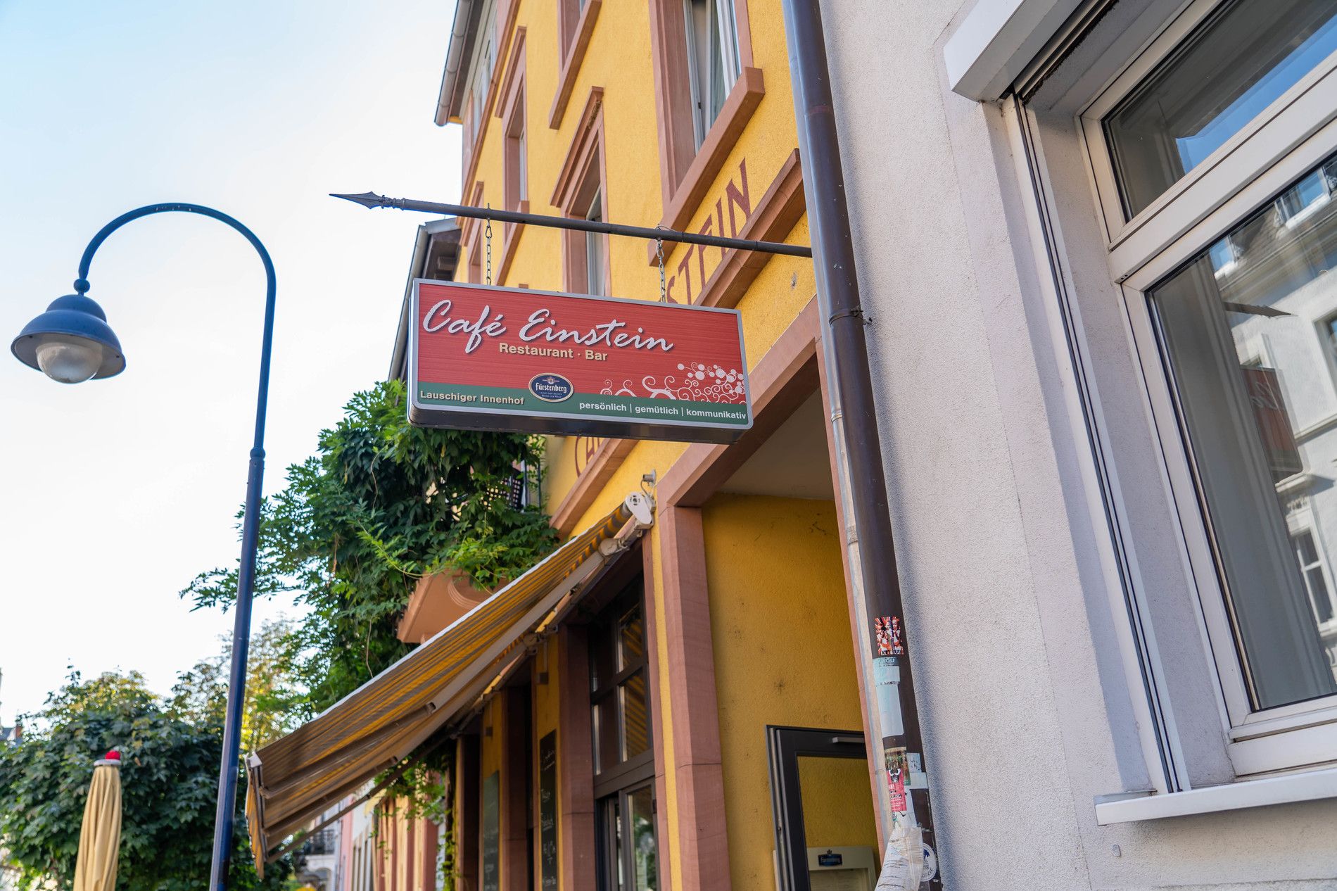 Ein gelbes Gebäude in Freiburg mit einem Schild des Café Einstein. Das Schild bewirbt das Café als Restaurant und Bar mit gemütlichem Innenhof.