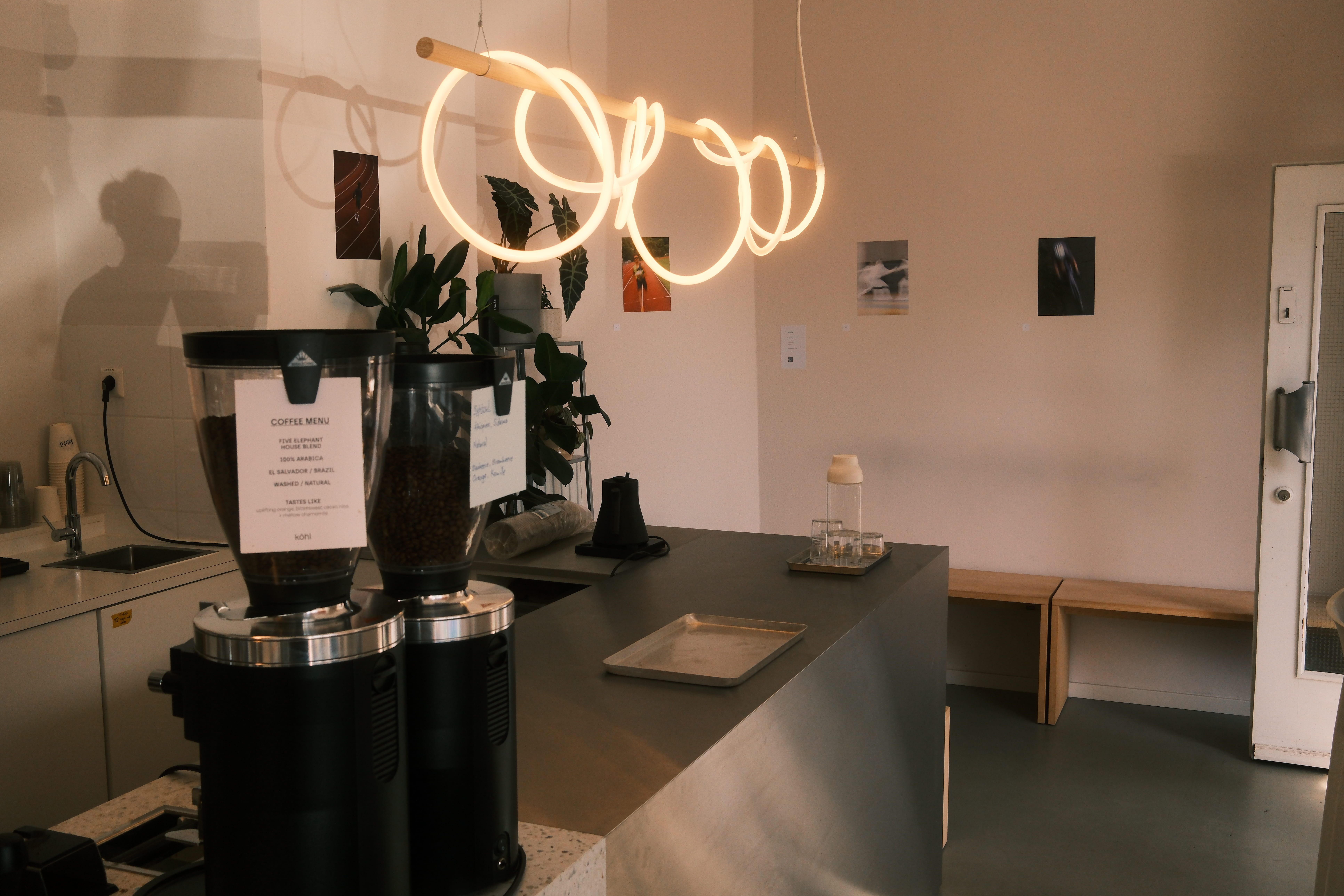 Das Kohi-Café zeigt eine minimalistische Theke mit Kaffeemühlen, Pflanzen und einer auffälligen Ringlampe.
