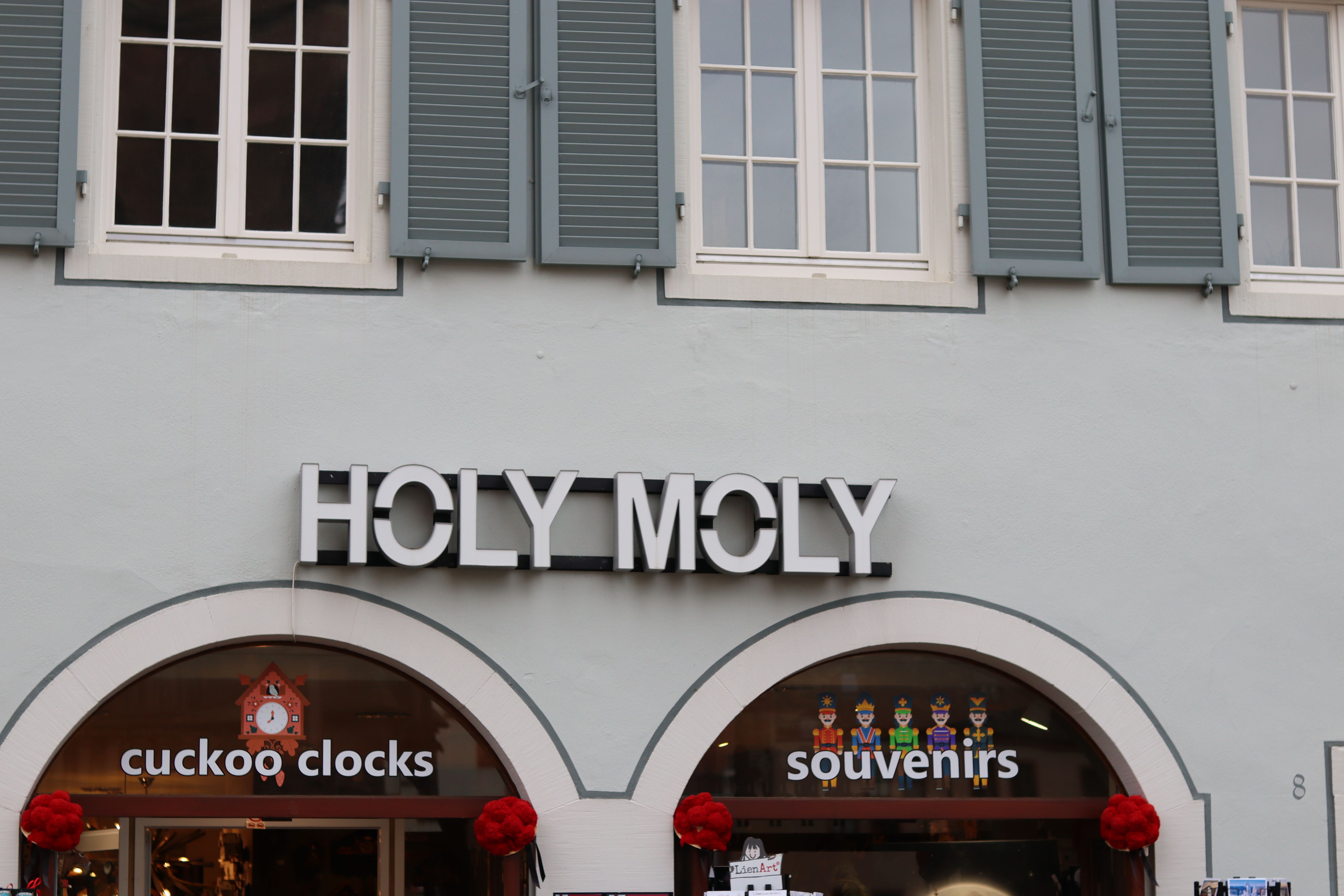 Fassade eines Geschäfts mit der Aufschrift 'HOLY MOLY', darunter Schaufenster mit 'cuckoo clocks' und 'souvenirs'.