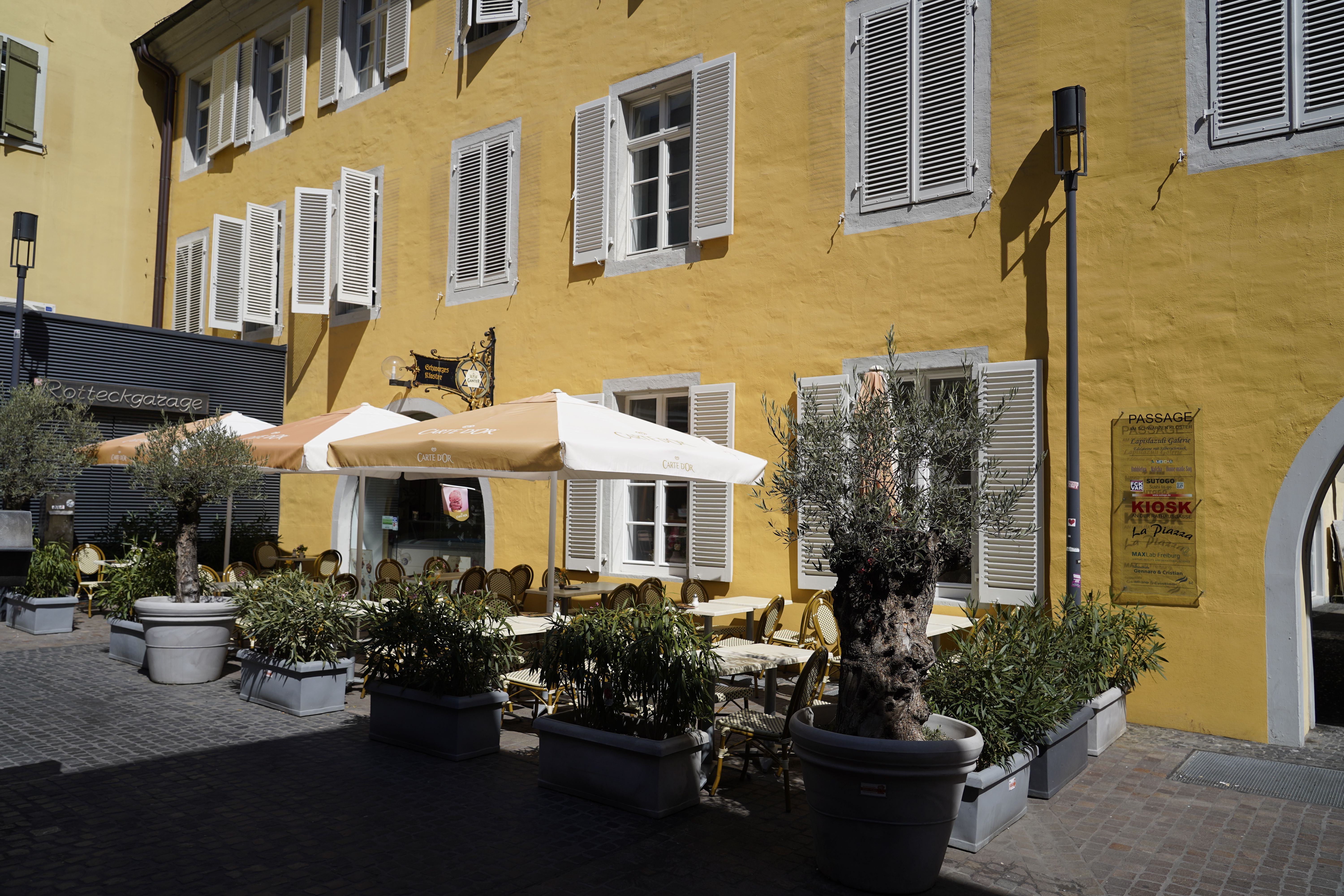 Ein Café mit gelber Fassade und weißen Fensterläden und einem schönen Außenbereich.