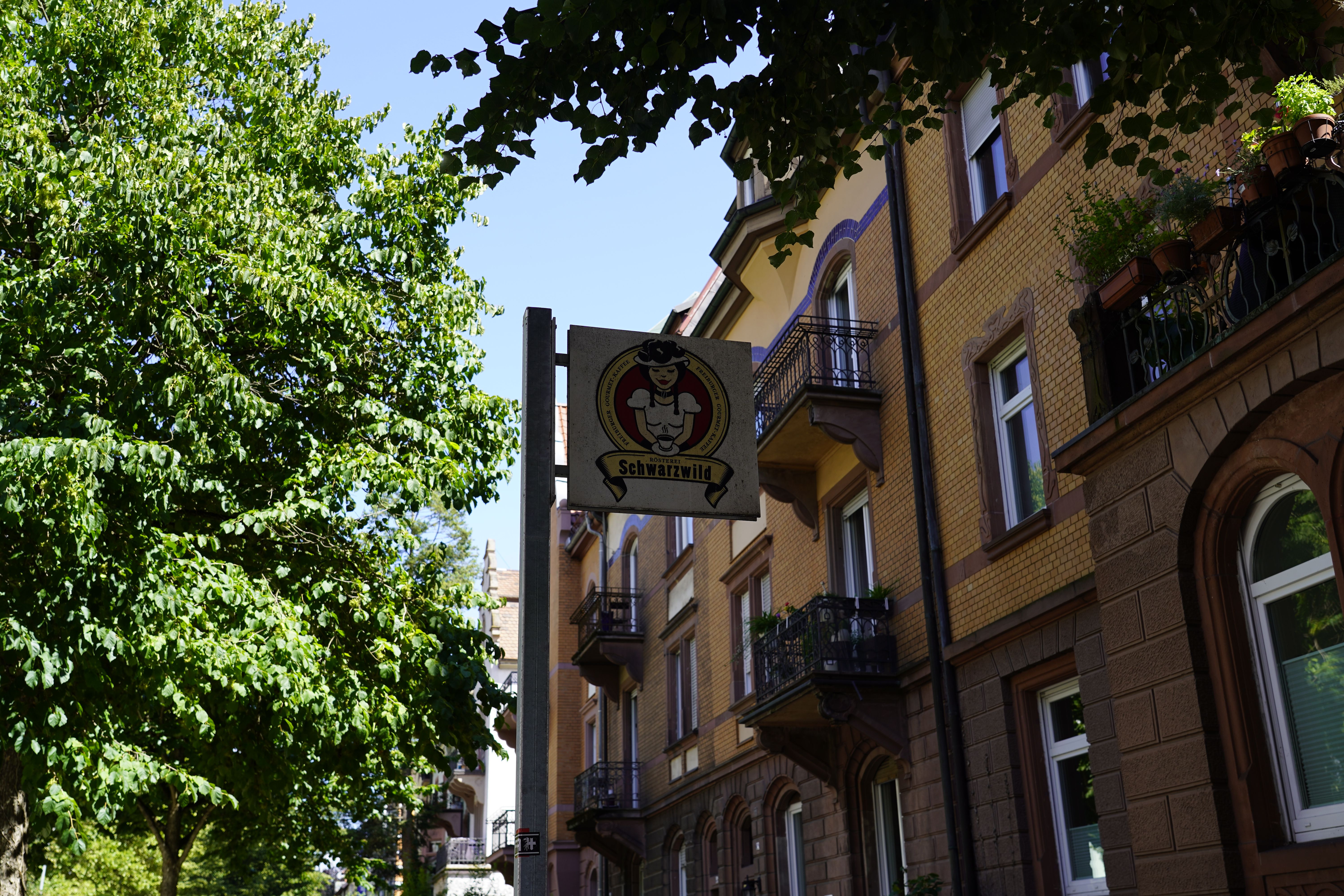 Schild mit 'Schwarzwild' an einem Gebäude, umgeben von Bäumen und Balkonen.