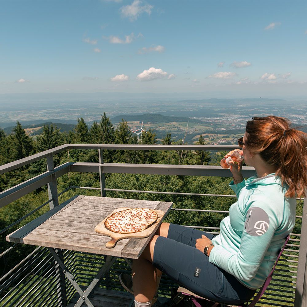 Die Bergstation Restaurant Frau sitz dort, trinkt aus einer Flasche und einem Flammkuchen vor sich