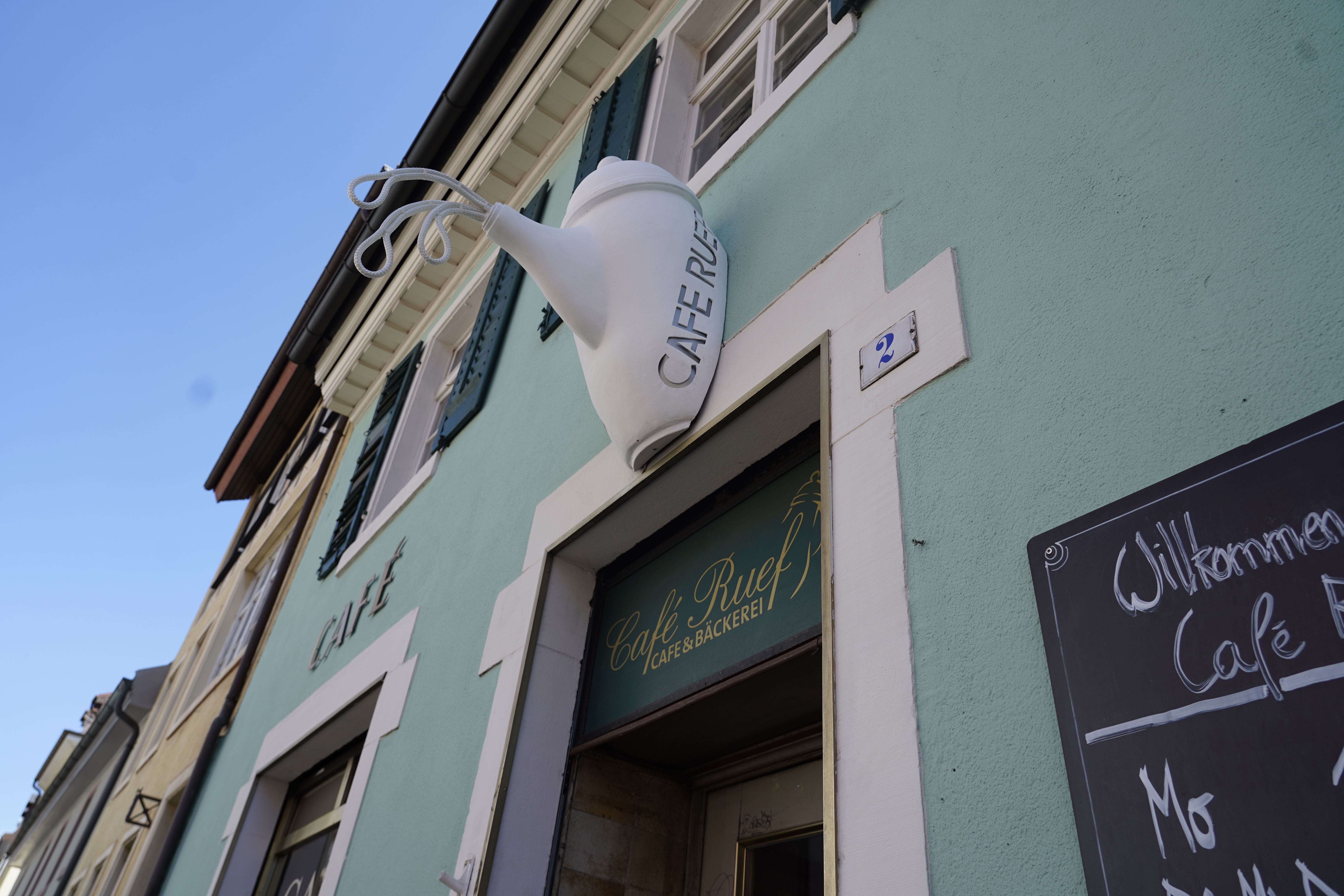 Außenansicht des Café Ruef mit einer großen Teekanne als Dekoration über dem Eingang. 