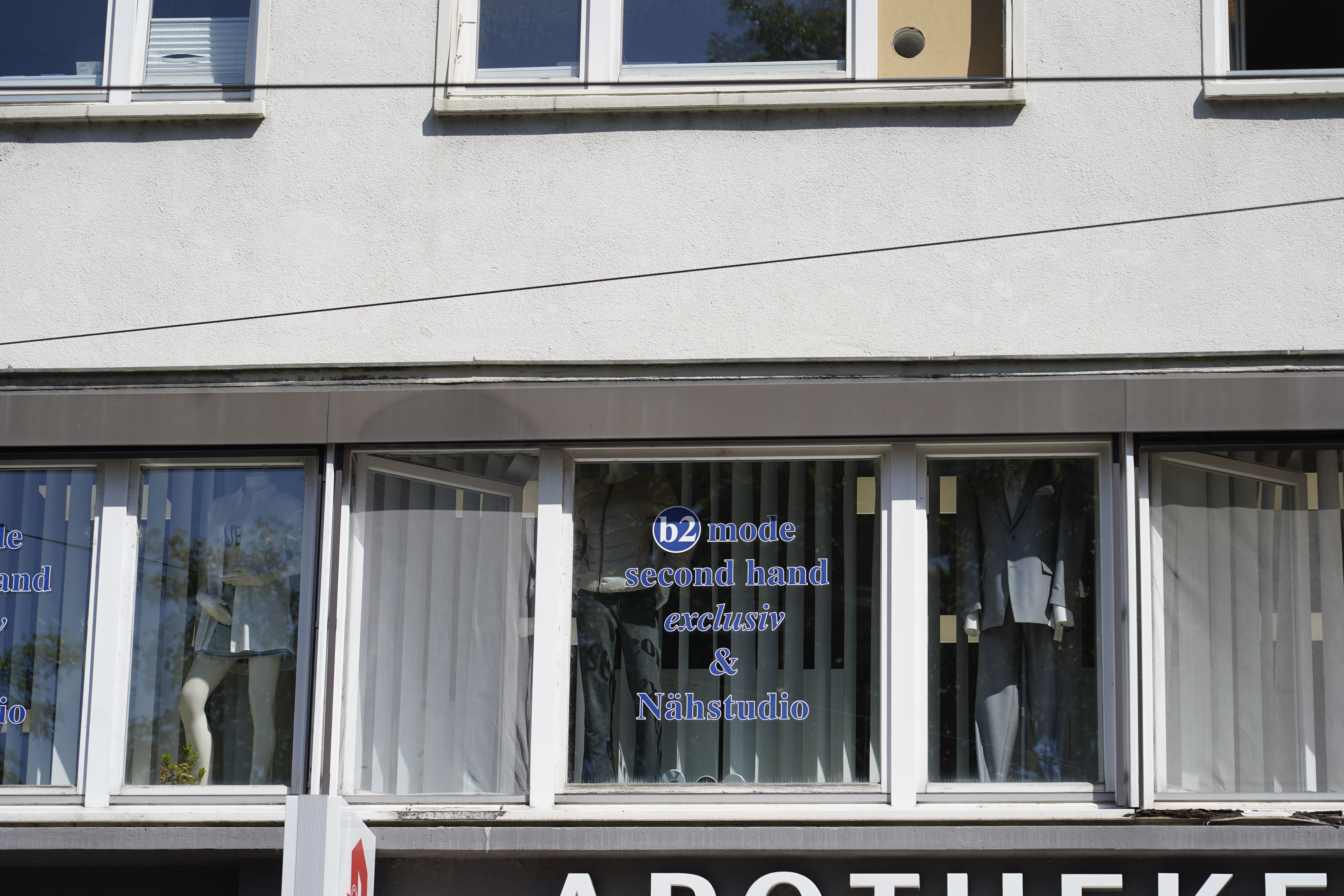 Schaufenster eines Second-Hand-Ladens mit der Aufschrift 'b2 mode second hand exclusiv & Nähstudio'. Im Fenster sind Schaufensterpuppen zu sehen.