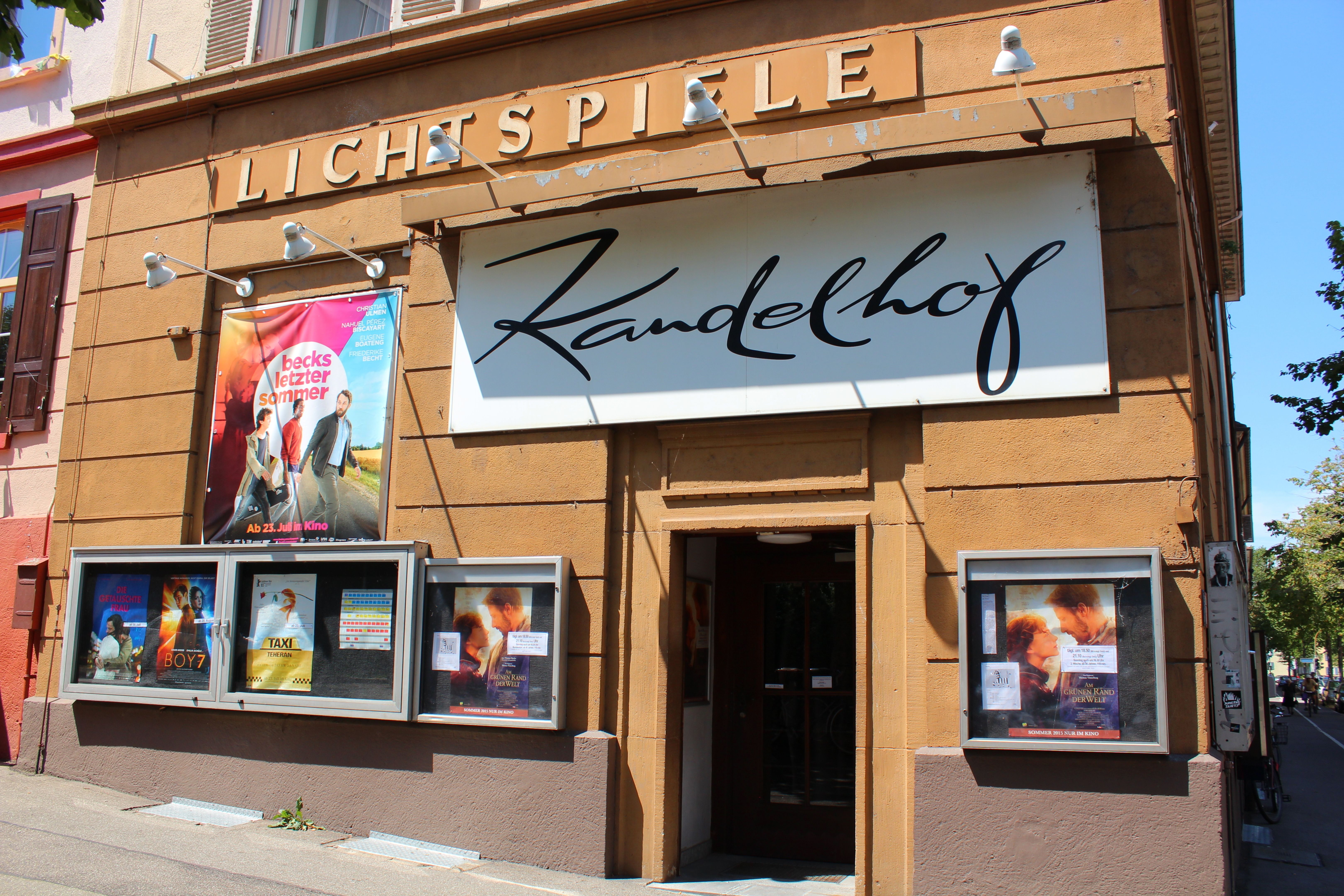 Eingang des Kinos Kandelhof in Freiburg. An der Fassade sind Filmplakate und ein großes Schild mit dem Namen des Kinos angebracht.