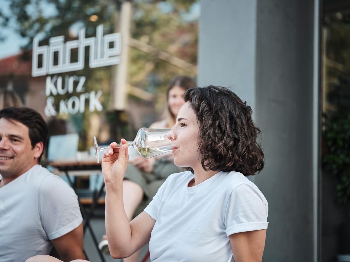Junge Frau trinkt einen Wein vor dem Bächle Café 