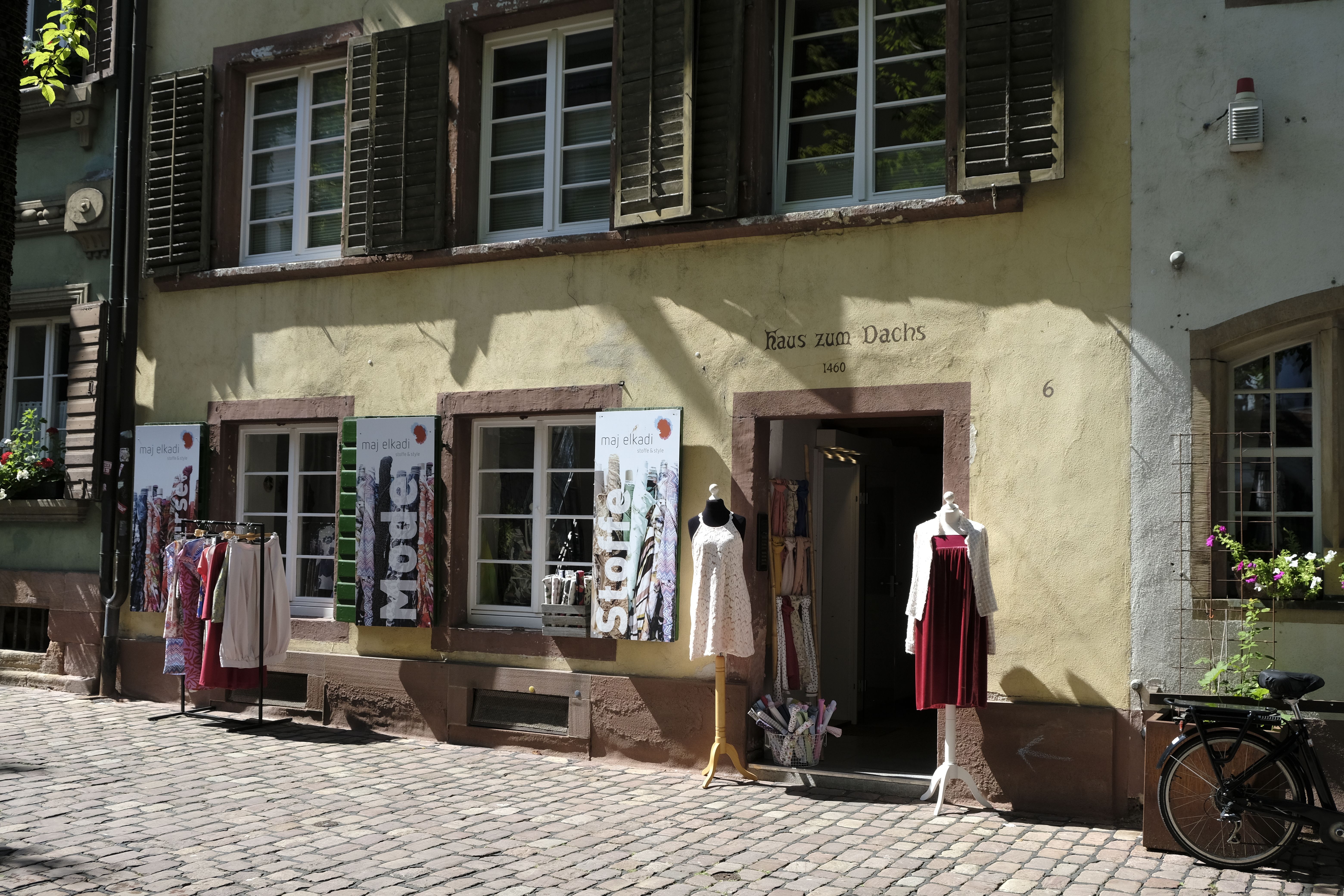 Stoffgeschäft in historischem Gebäude mit Schaufensterpuppen und Kleidung im Freien.
